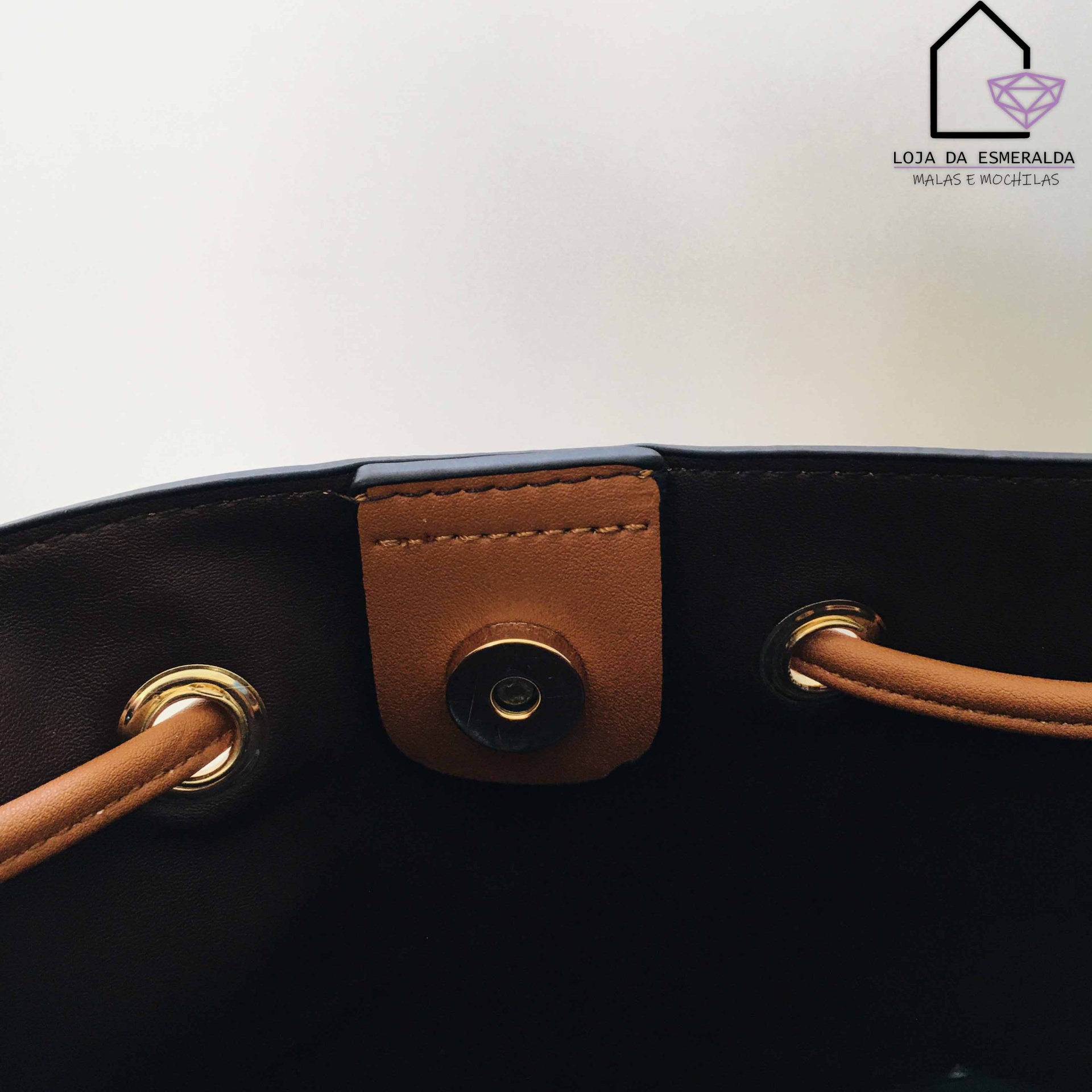 Interior de mala preta com fecho magnético castanho, ilhós dourados e alças castanhas