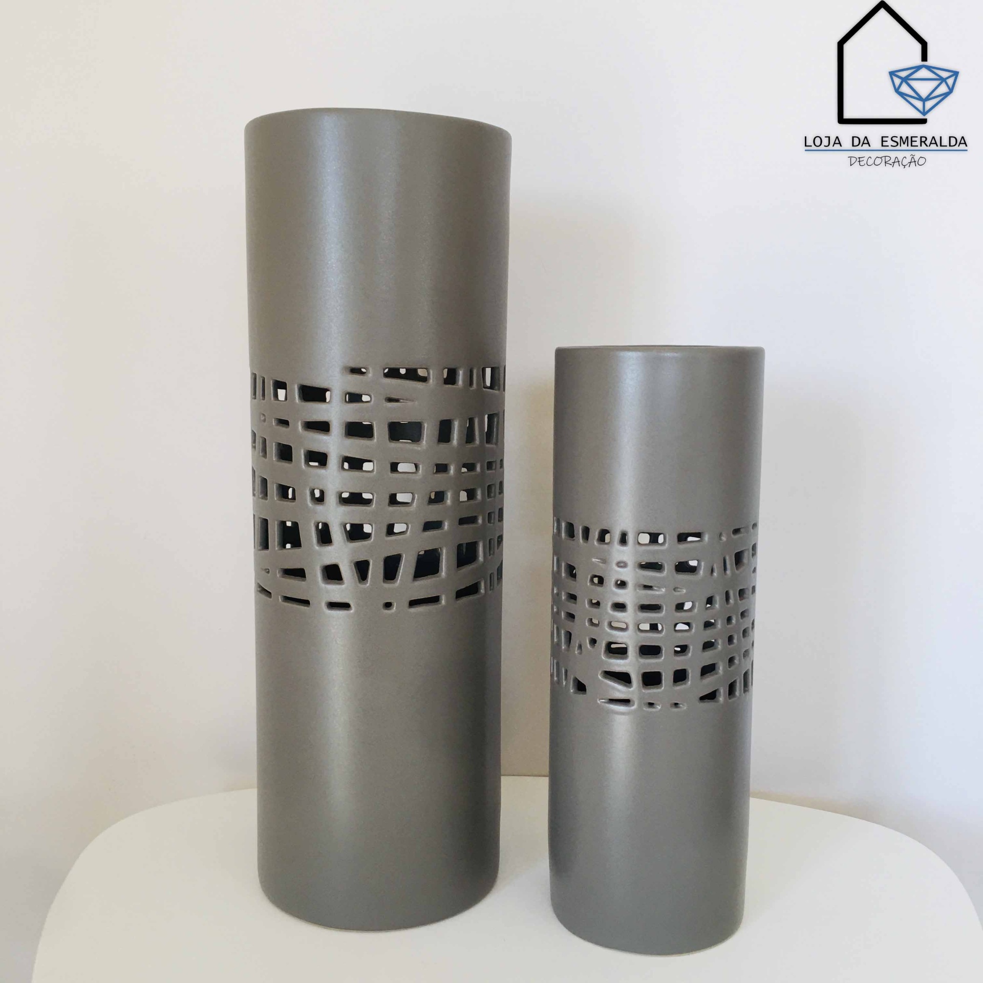 Dois vasos cilíndricos cinzentos com padrão geométrico vazado, colocados numa superfície branca.