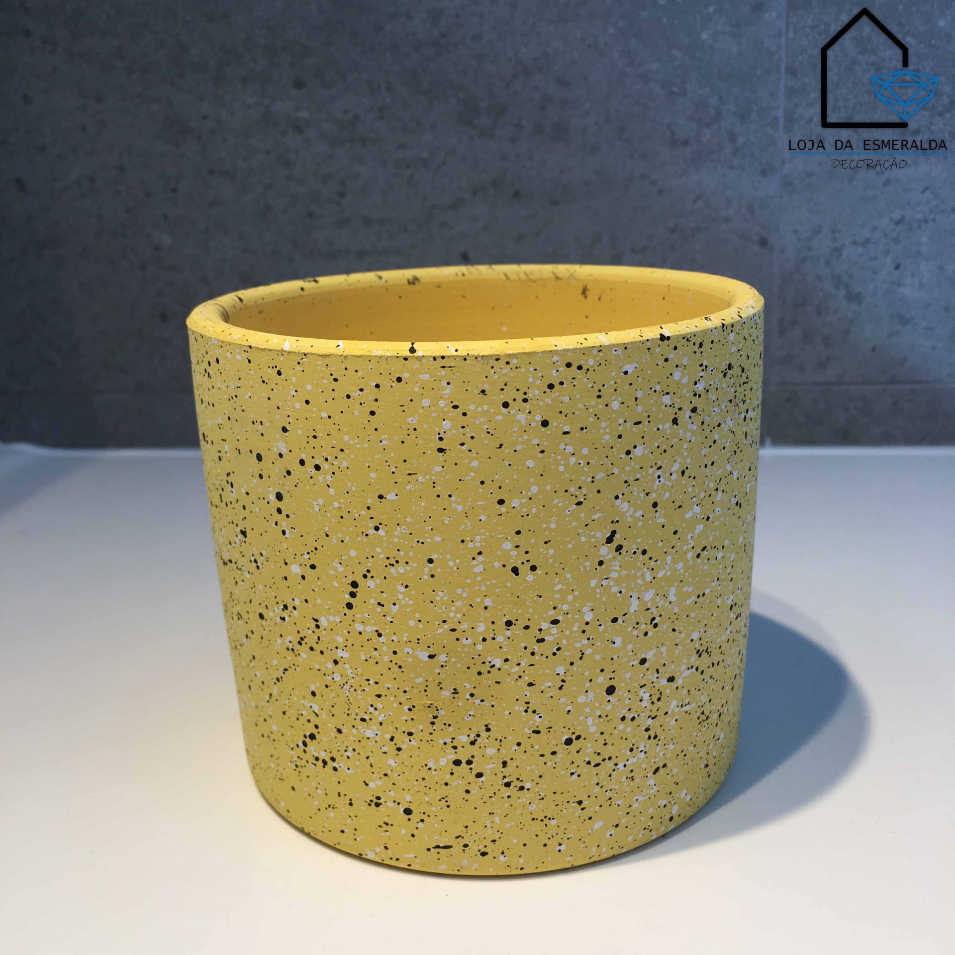 Vaso amarelo salpicado em superfície branca com fundo cinzento