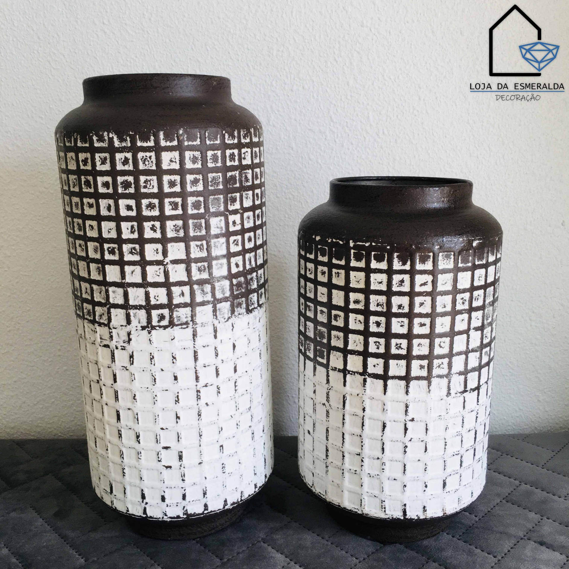 Dois vasos cerâmicos com padrão quadriculado branco e castanho escuro sobre superfície acolchoada cinza