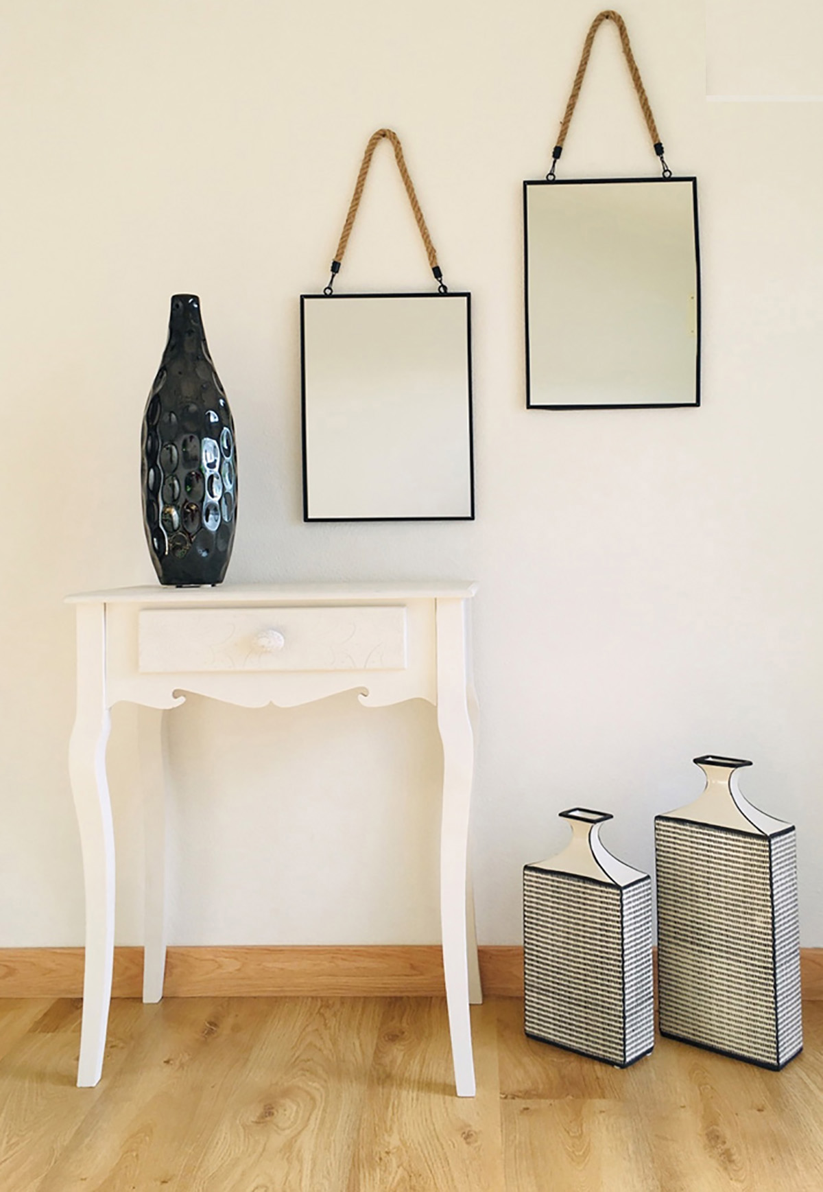 Mesa branca com gaveta, dois espelhos pendurados com corda, vaso preto texturizado em cima e dois vasos decorativos no chão