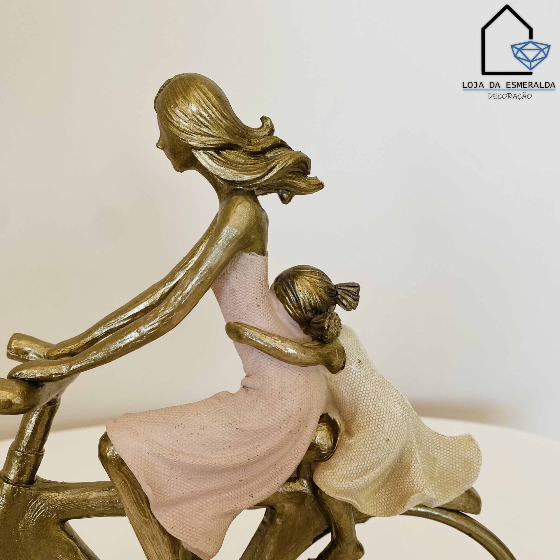 Estatueta metálica de mulher e menina numa bicicleta com vestidos rosa e creme