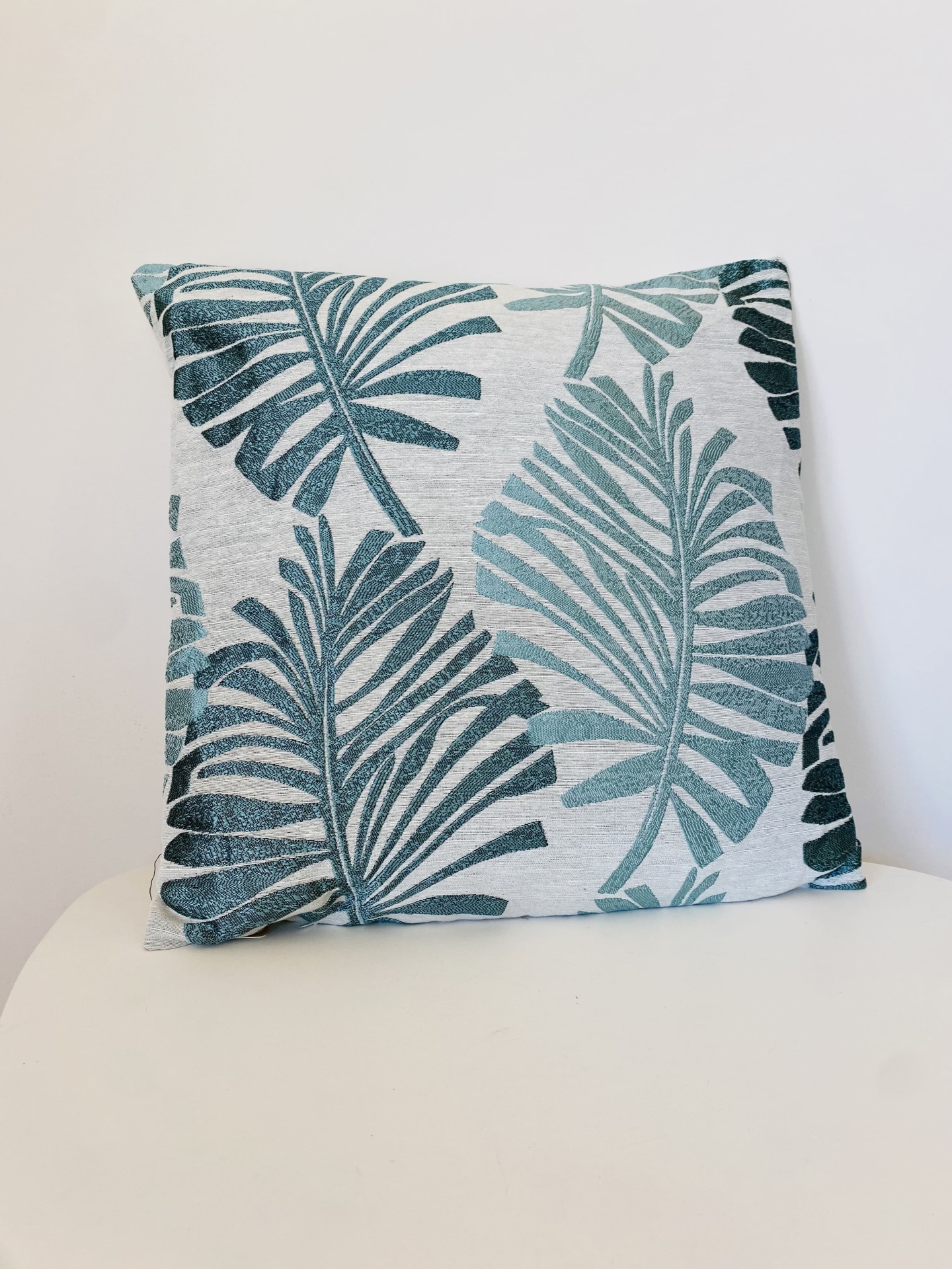 Almofada decorativa com padrão de folhas verdes em fundo cinza claro