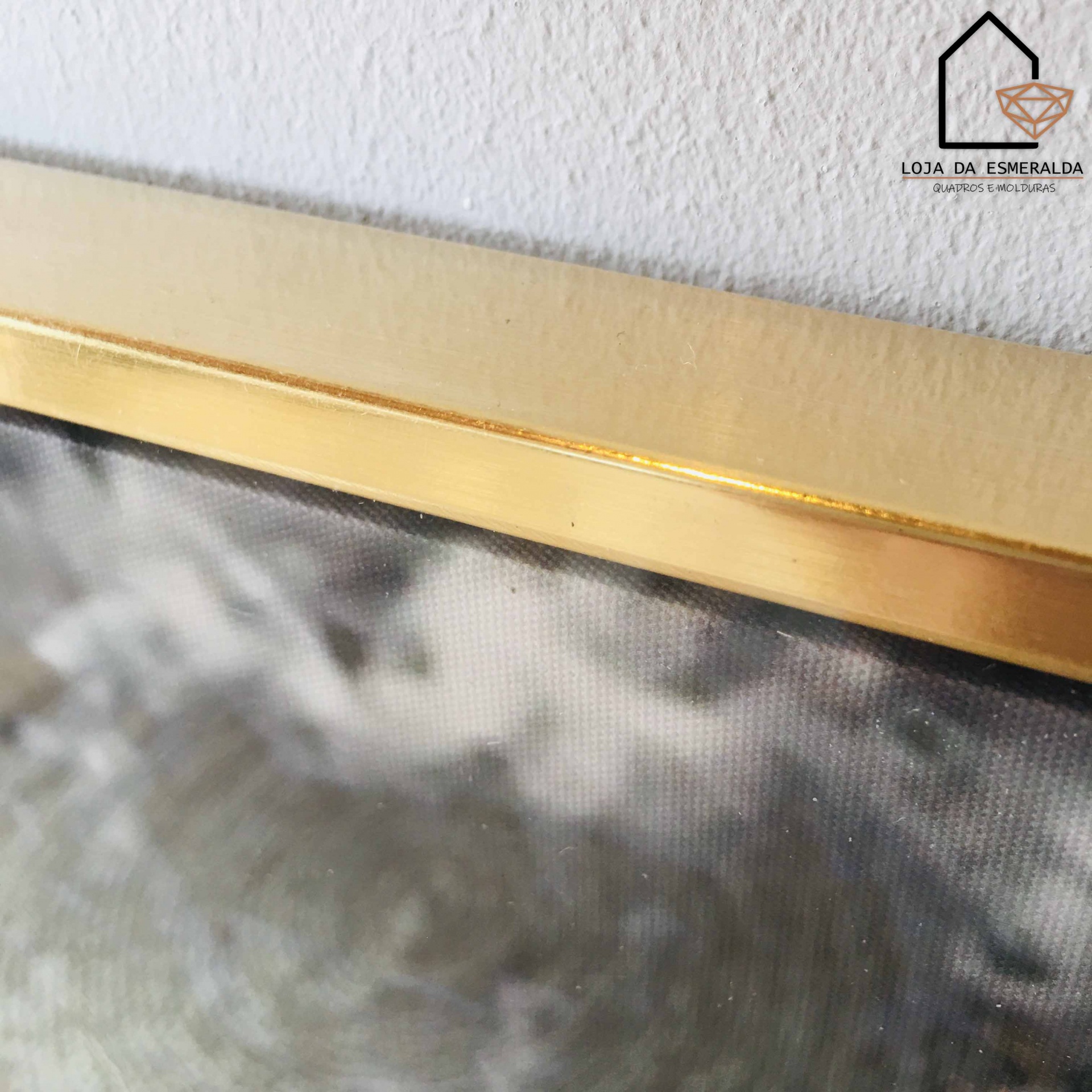 Moldura dourada com vidro pendurada numa parede branca, logótipo e texto no canto superior direito