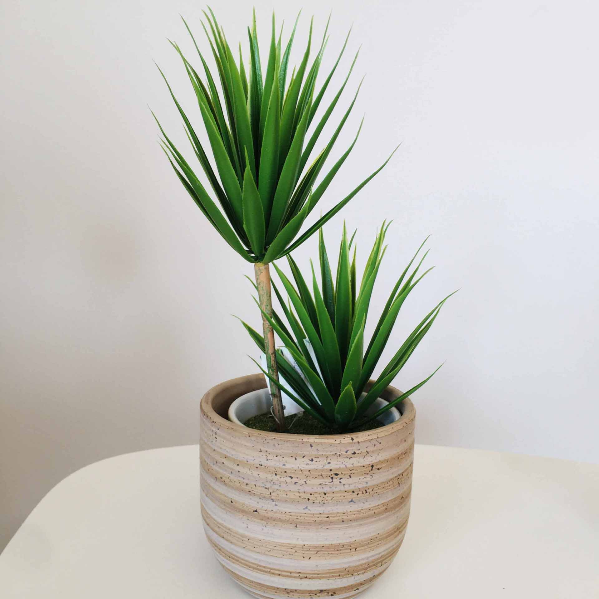 Planta artificial verde em vaso cerâmico riscado sobre mesa branca