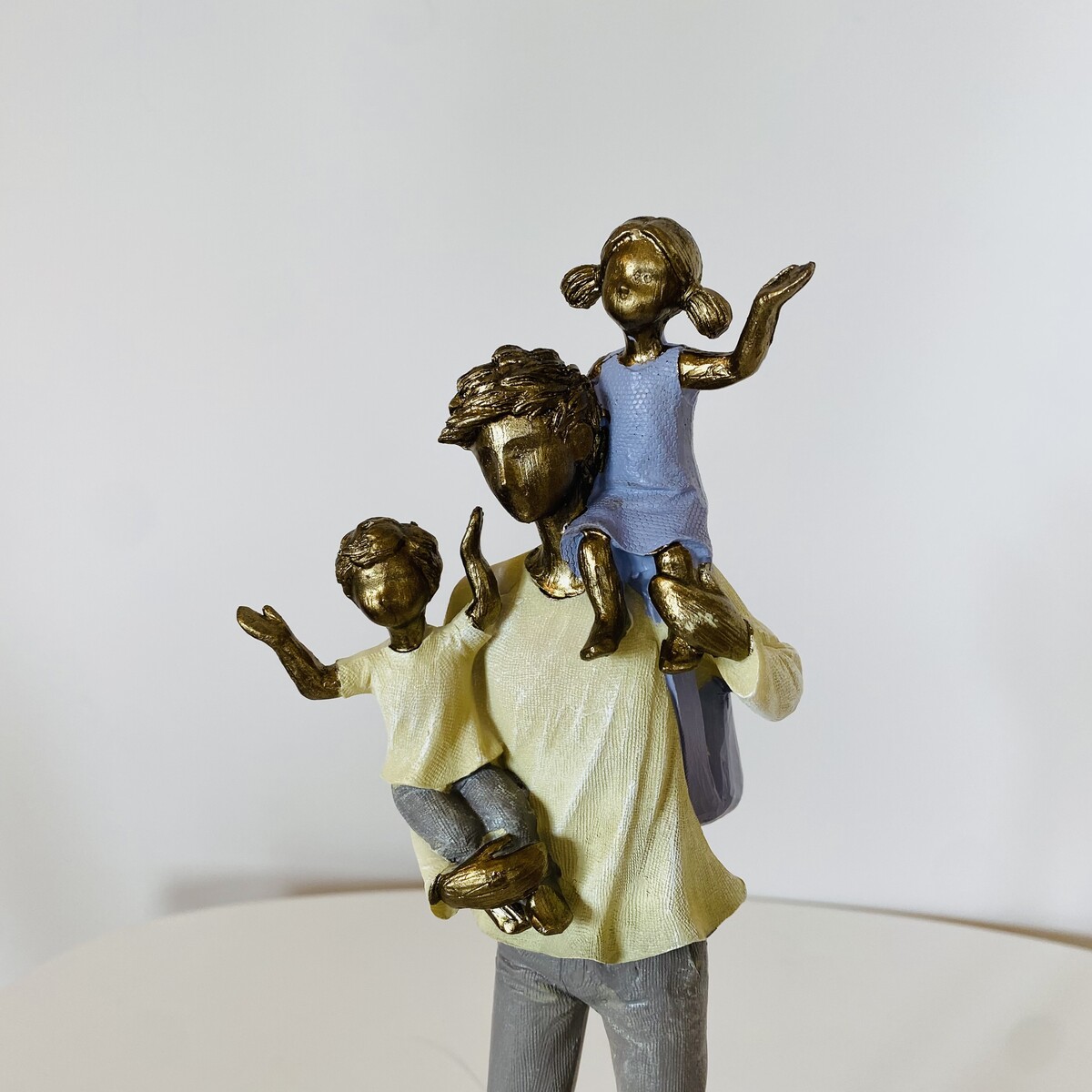 Estátua decorativa em resina com figura adulta e duas crianças, com cores azul, amarelo e dourado.