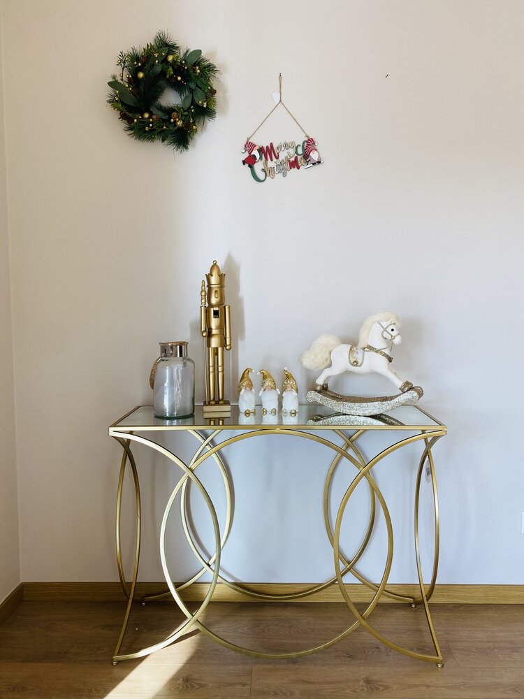Mesa de consola dourada decorada com objetos natalícios e ornamentos na parede com tema natal