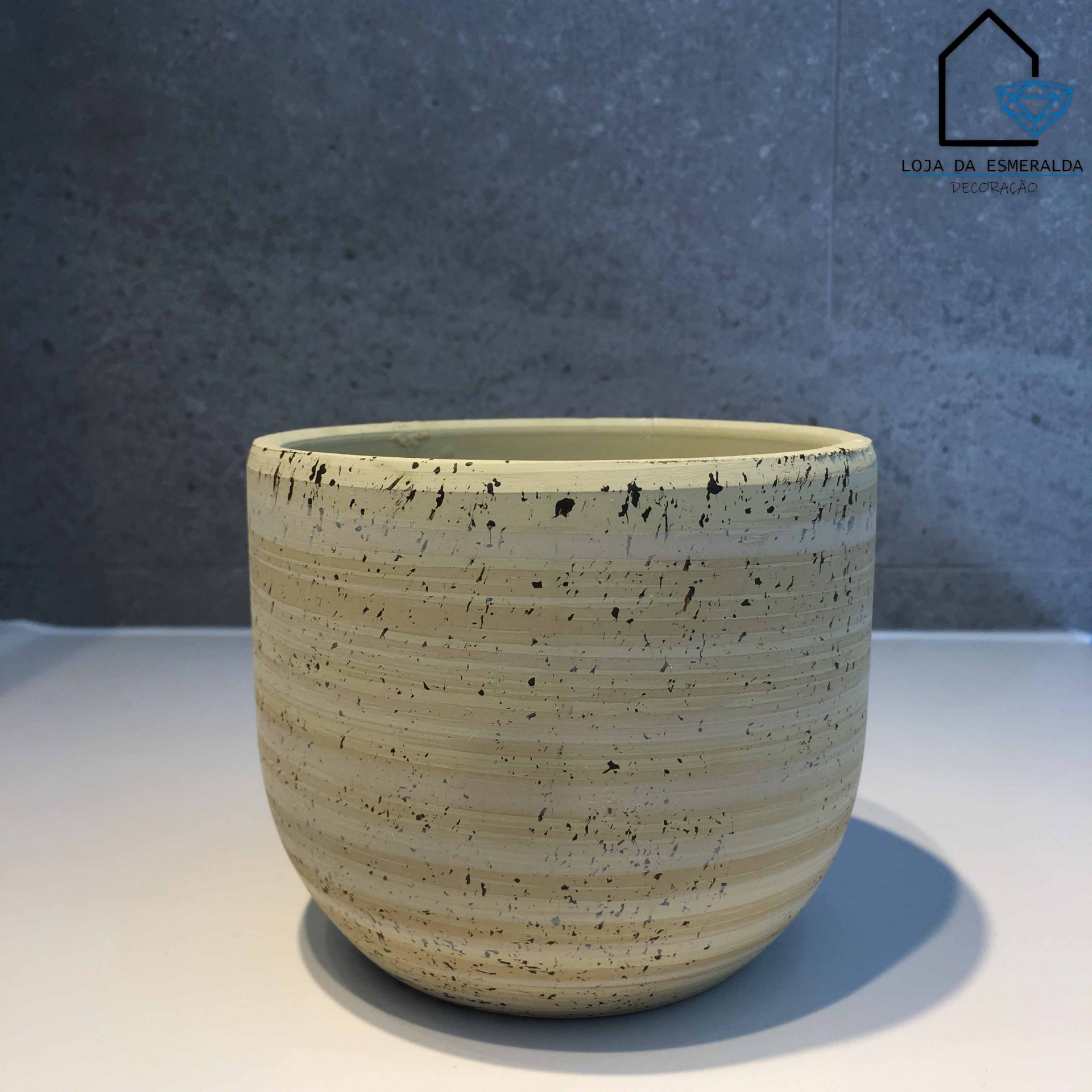 Vaso de cerâmica creme com pintas pretas sobre superfície branca e fundo cinzento