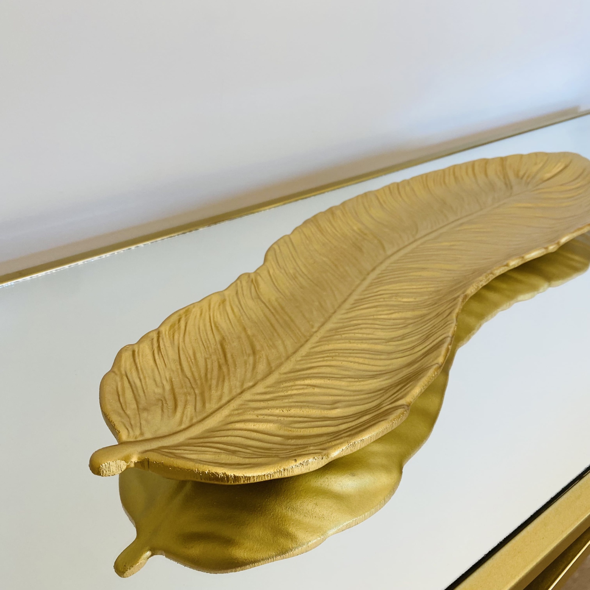 Prato decorativo dourado em forma de folha com textura sobre superfície espelhada.
