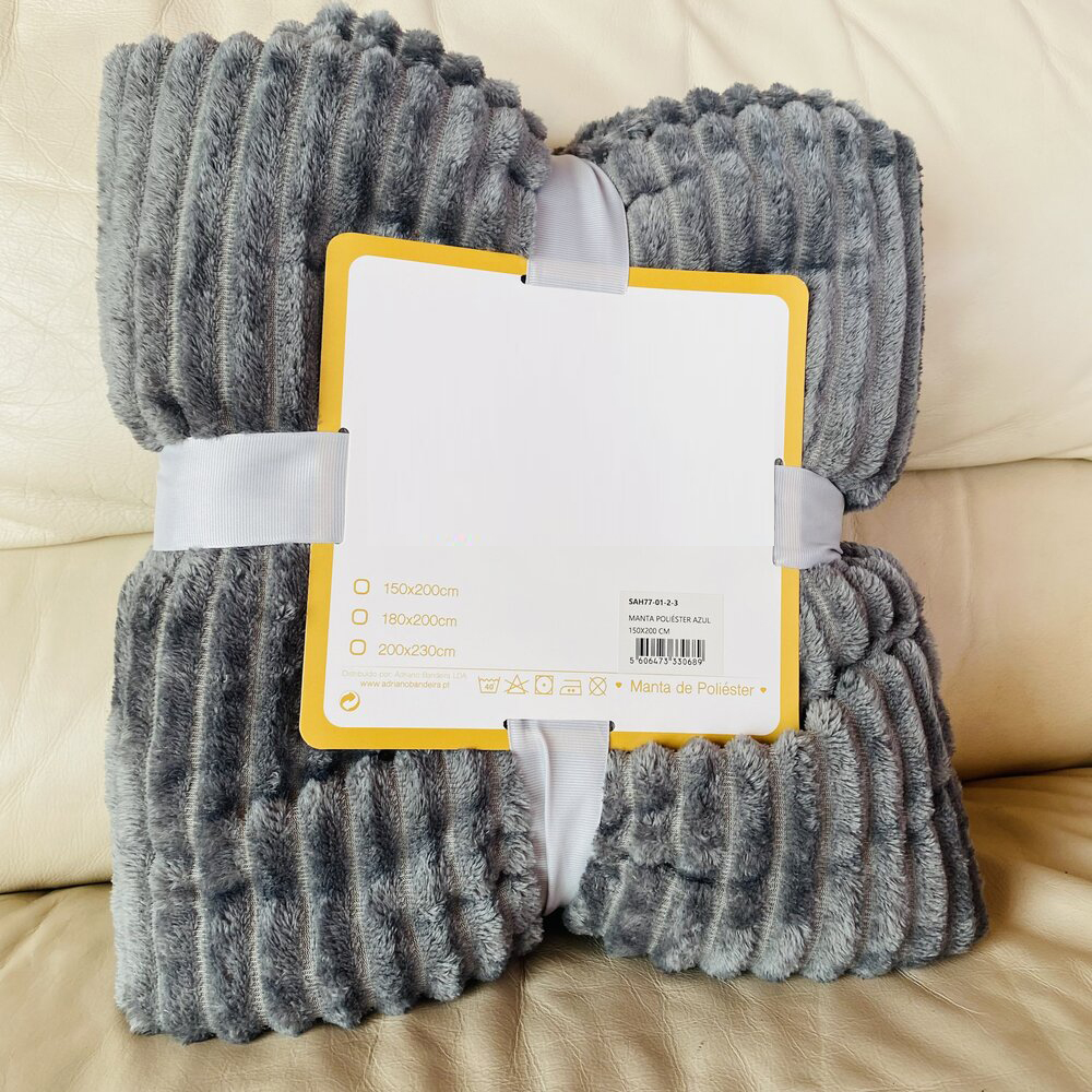 Manta cinza enrolada com etiqueta e faixa branca sobre sofá bege