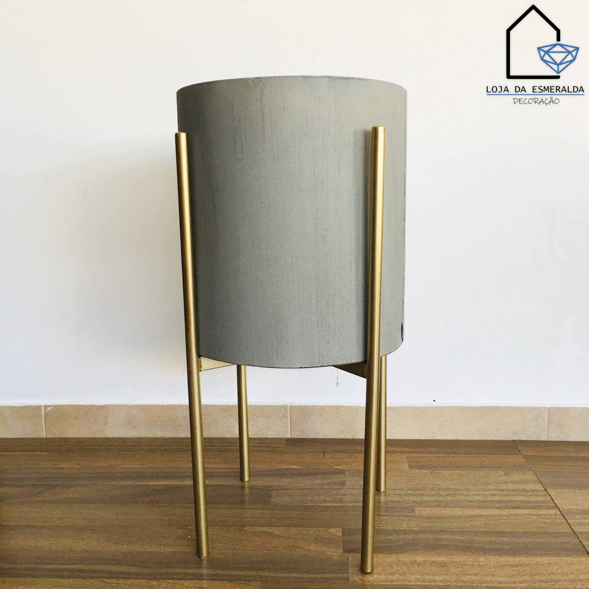 Vaso cinzento com suporte metálico dourado em chão de madeira
