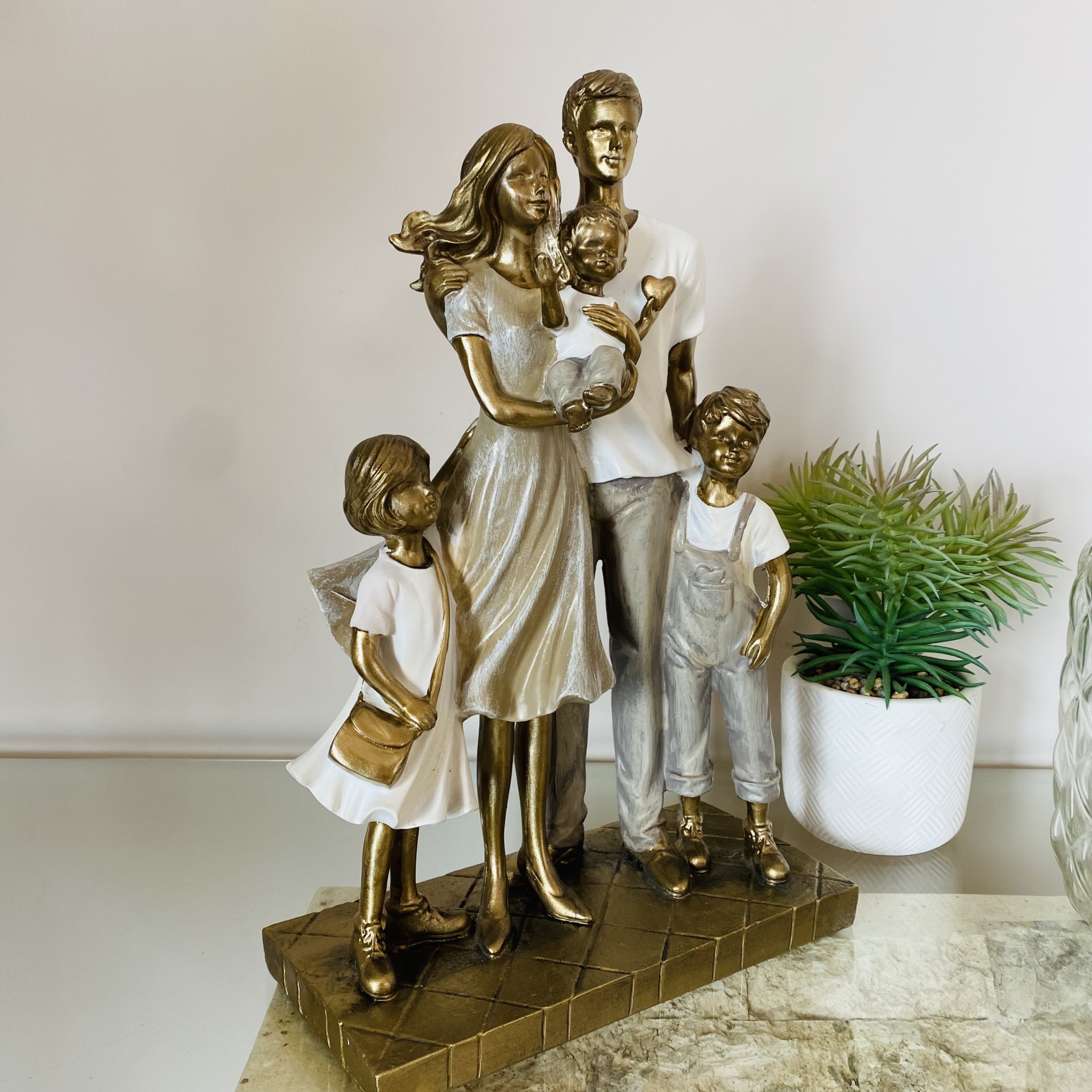 Estátua decorativa de família dourada e branca com quatro membros e bebé numa base castanha