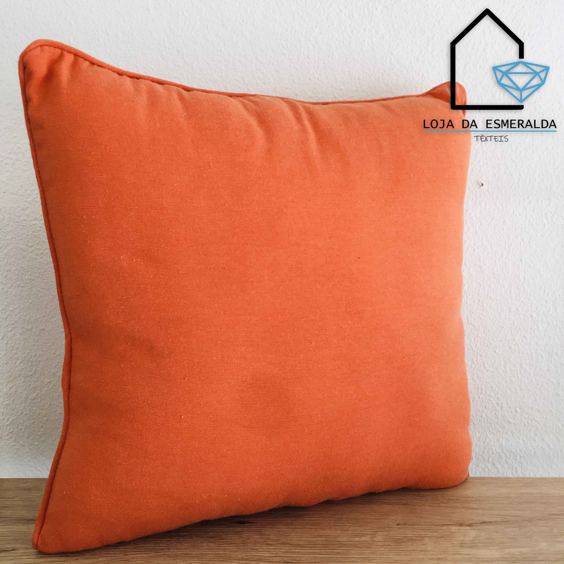 Almofada laranja com logótipo LOJA DA ESMERALDA junto à parede branca