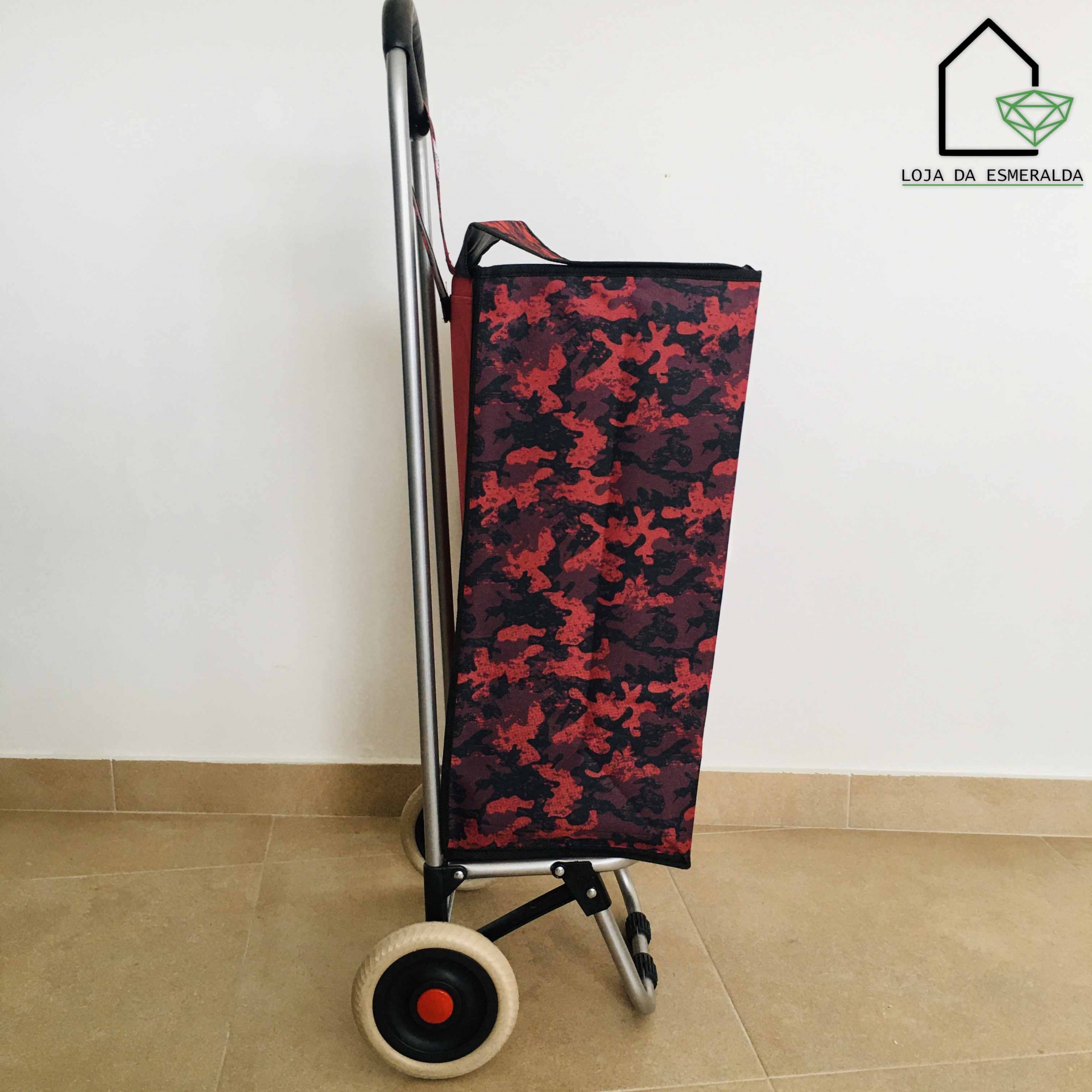 Carrinho de compras vermelho com padrão camuflado, estrutura metálica e rodas em chão de azulejo bege