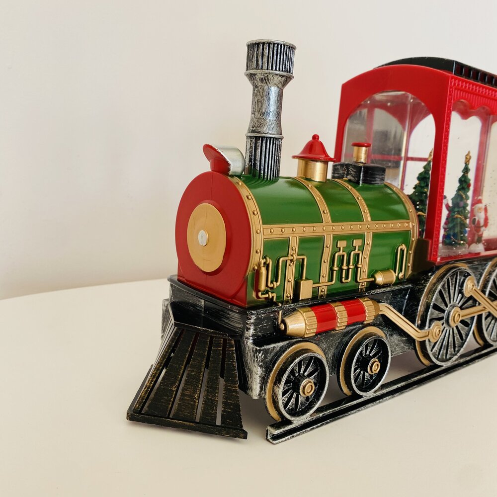 Modelo decorativo de comboio com locomotiva verde, vermelho e dourado sobre superfície branca