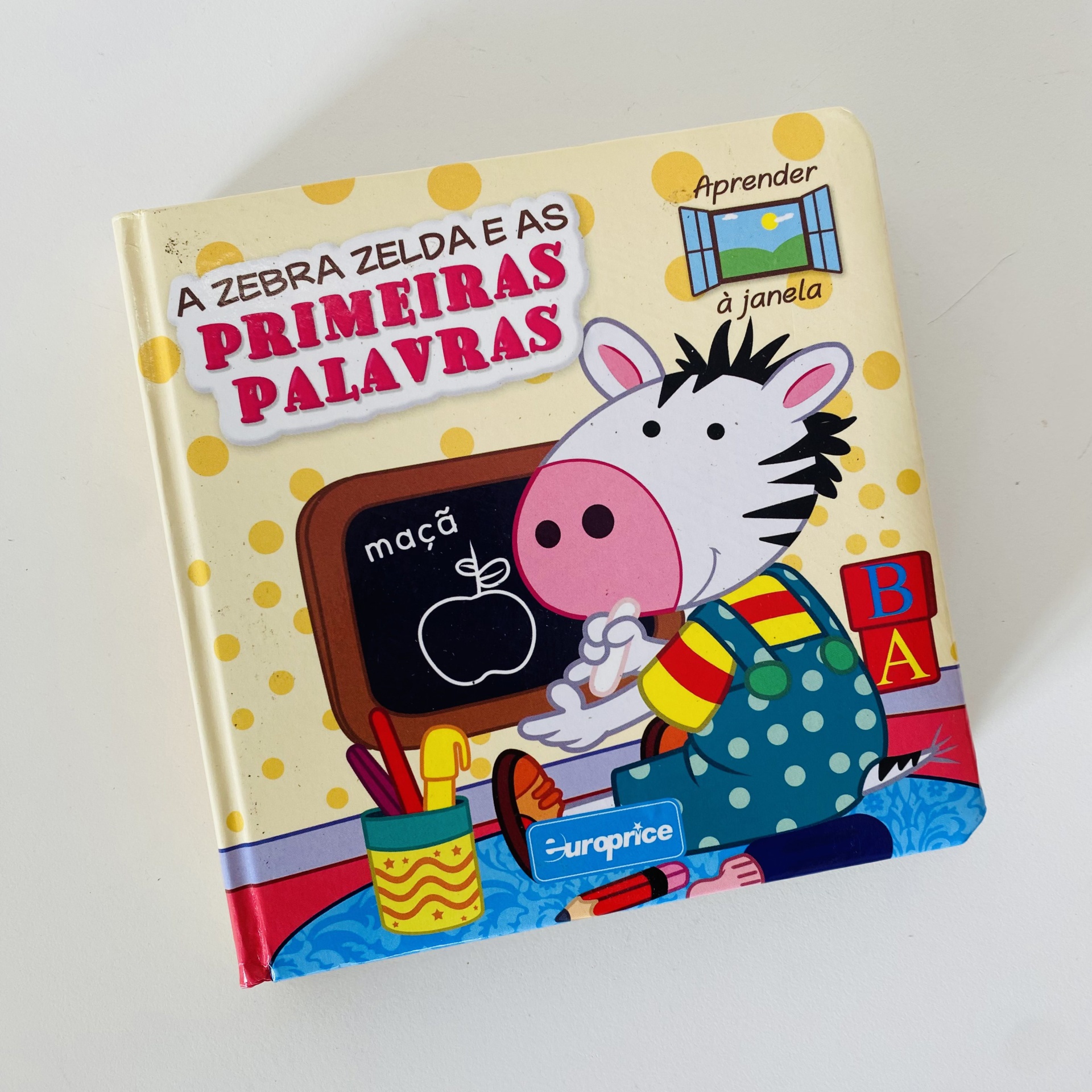 Capa de livro infantil A Zebra Zelda e as Primeiras Palavras com ilustração de zebra e quadro negro