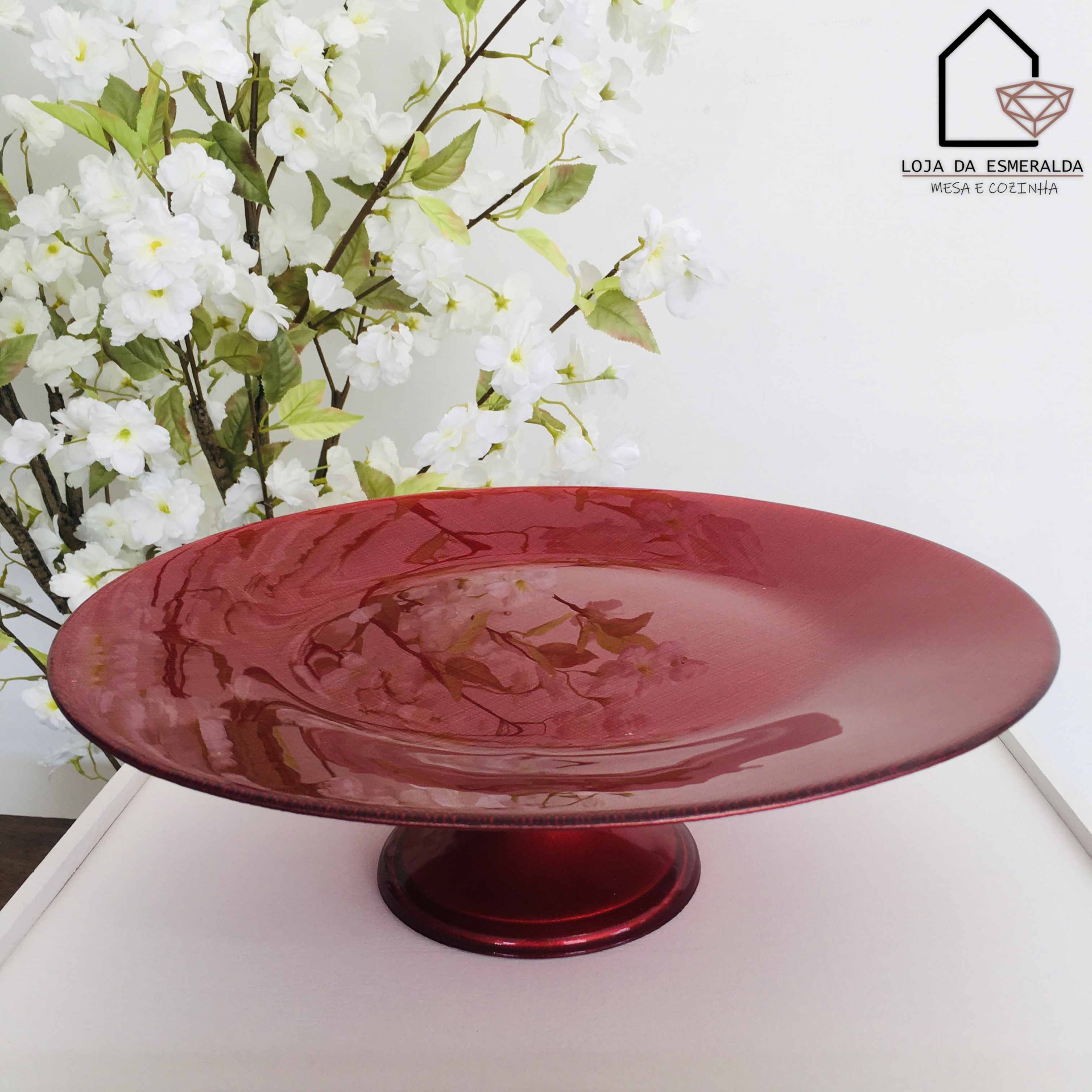 Prato decorativo de vidro vermelho sobre suporte com flores ao fundo