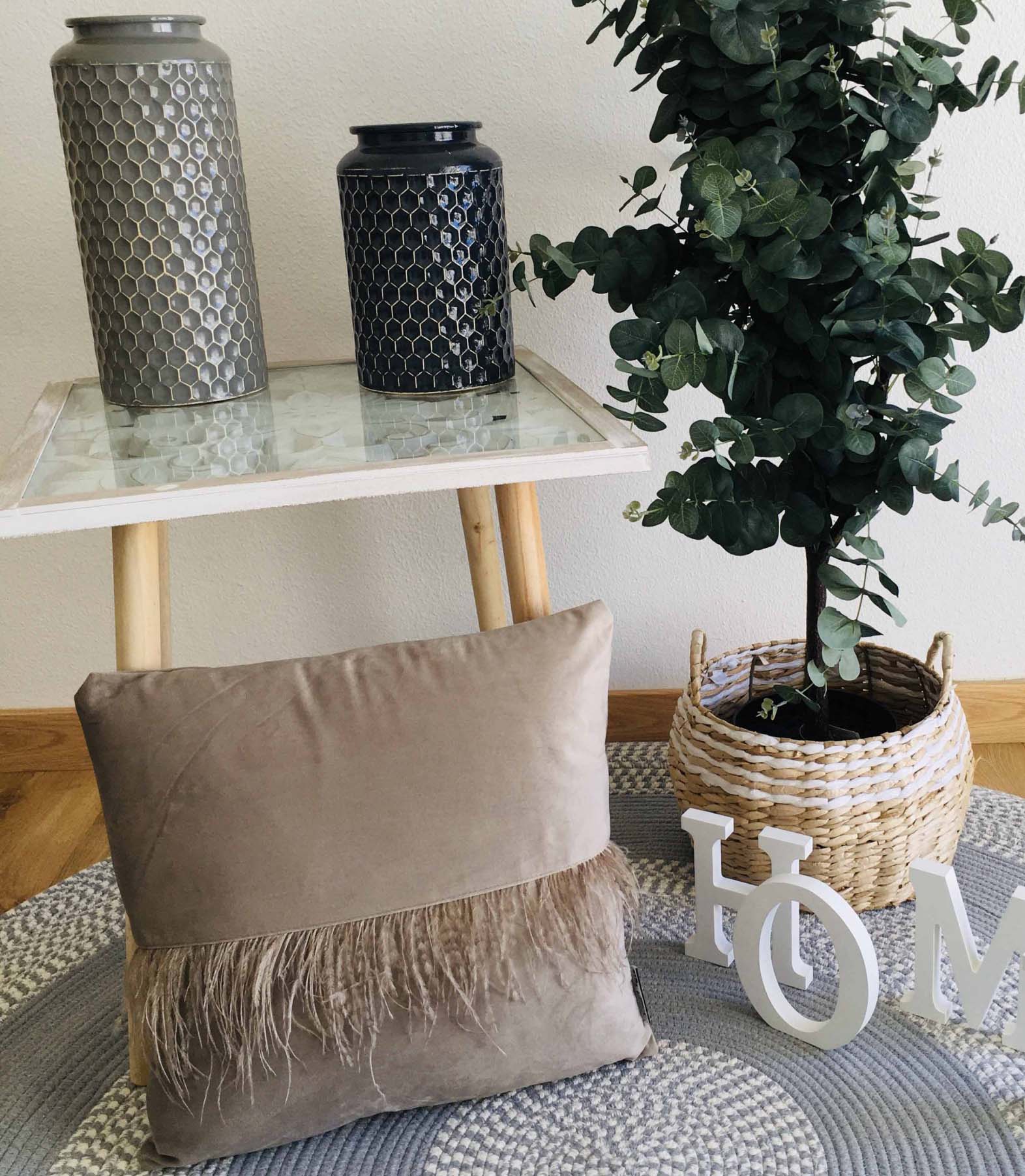 Mesa com vasos cerâmicos, almofada com franjas, planta em vaso de vime e tapete redondo cinza