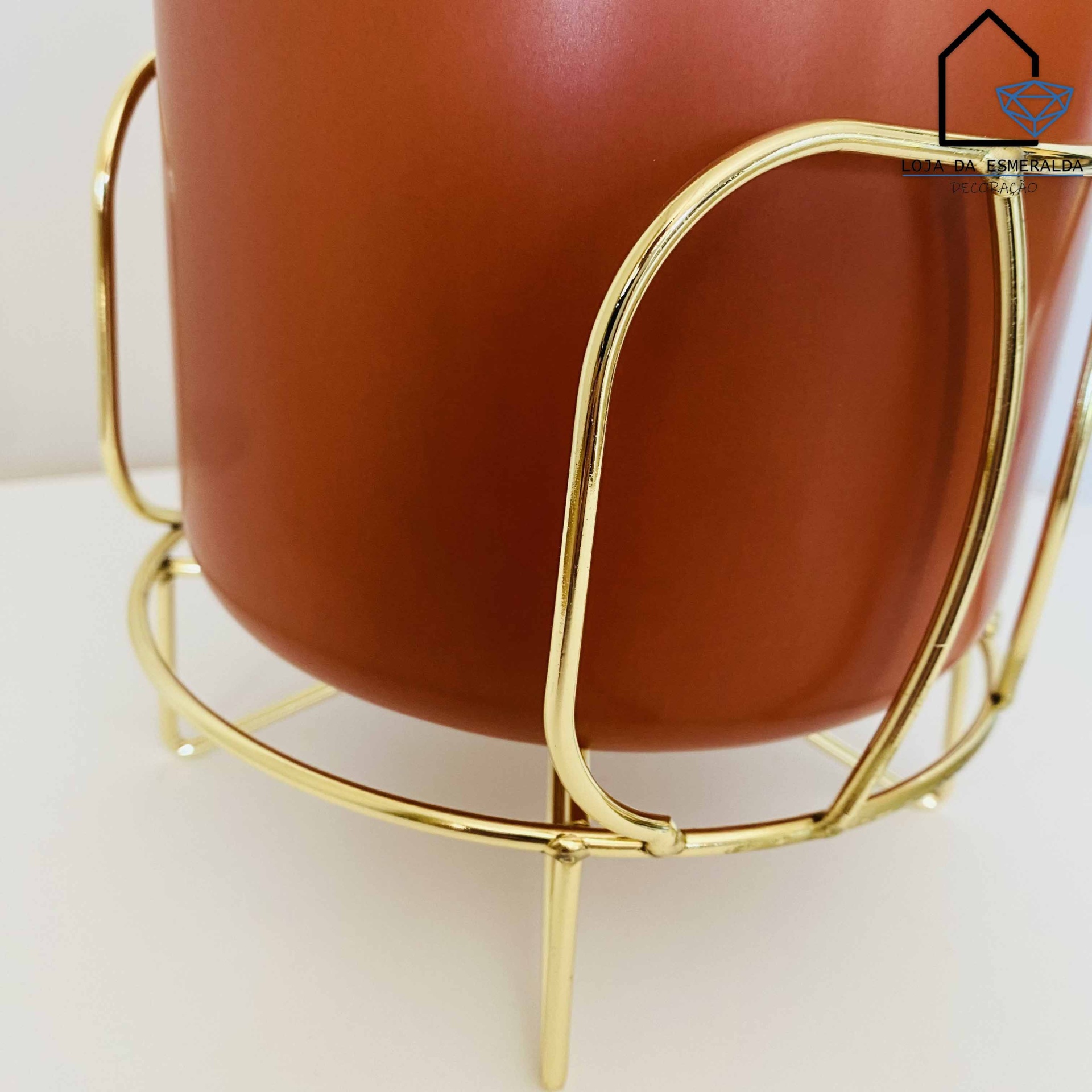 Vaso ferrugem com suporte metálico dourado em superfície branca