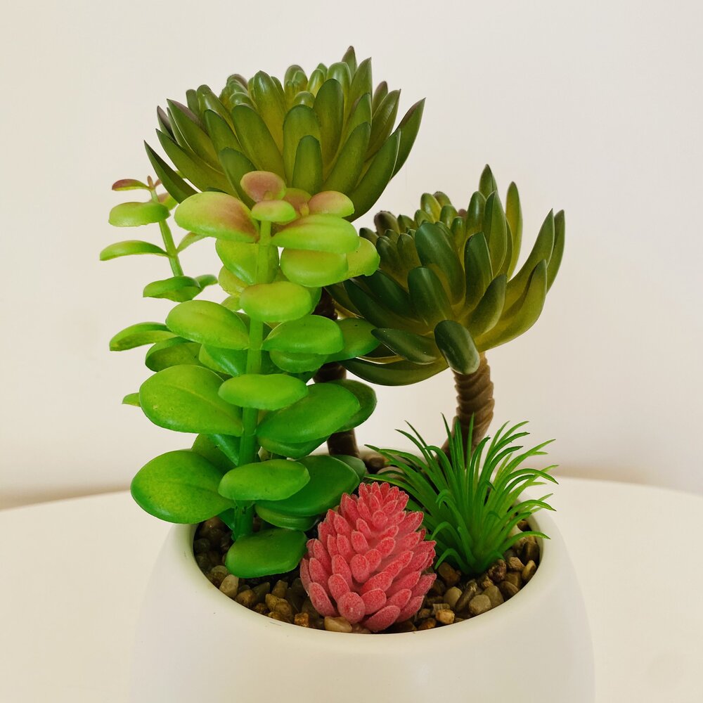 Vaso branco com plantas suculentas artificiais verdes e rosa em pedras decorativas