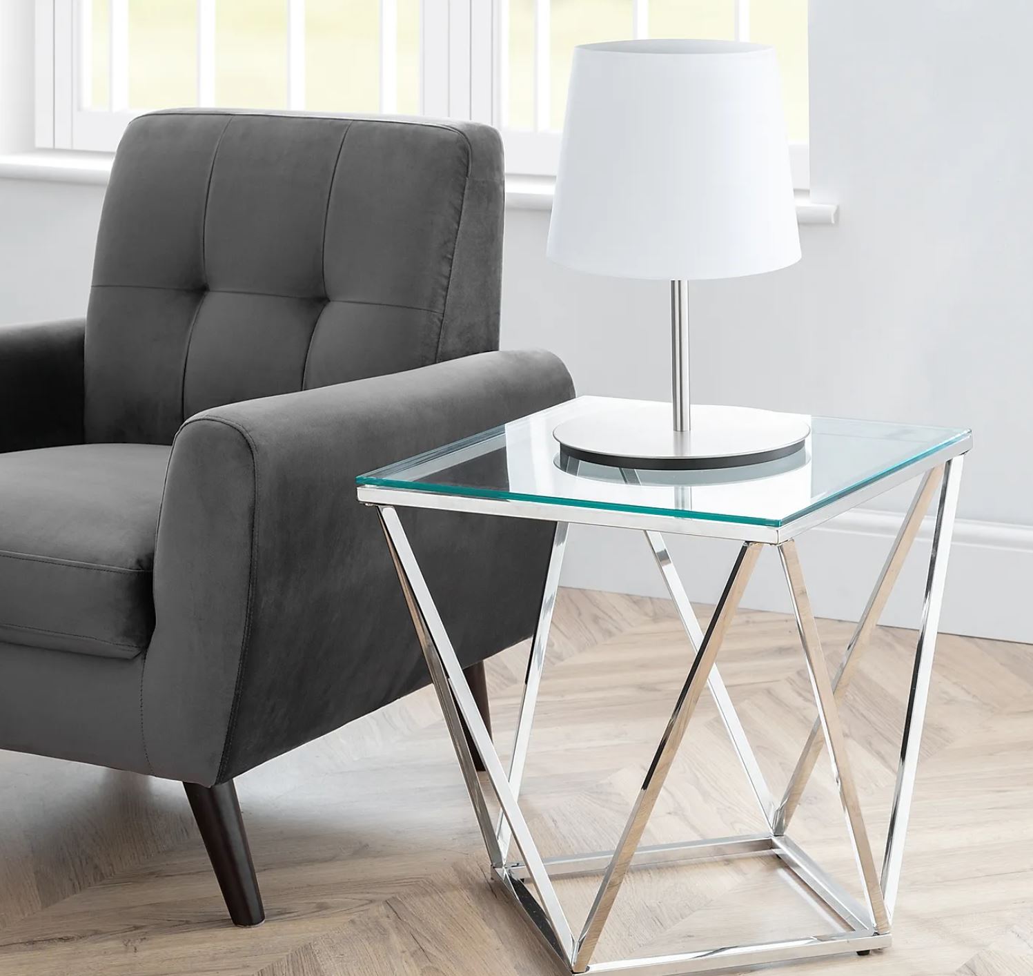 Cadeira cinzenta ao lado de mesa de apoio de vidro com lâmpada branca