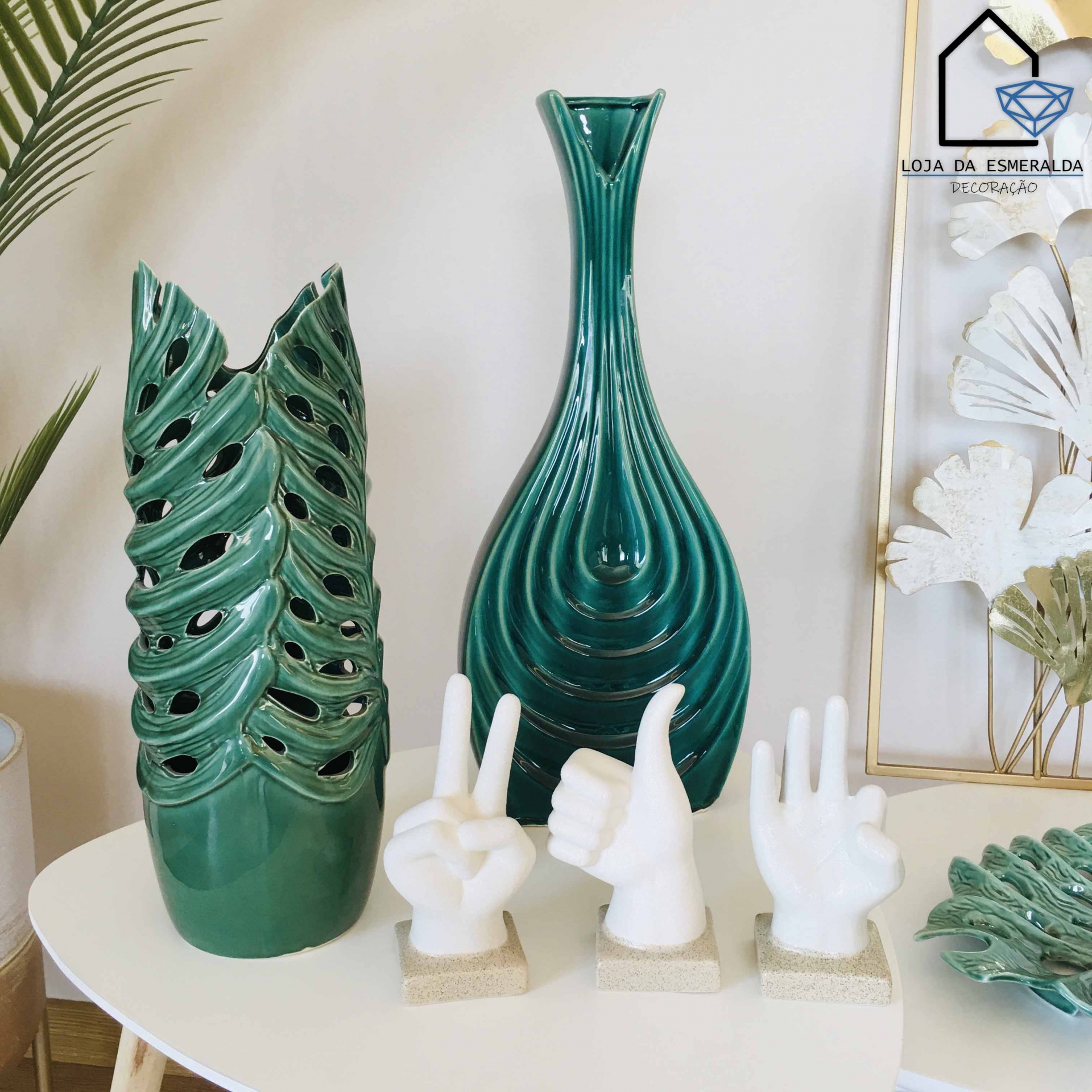 Vasos cerâmicos verdes e esculturas de mãos brancas numa mesa branca