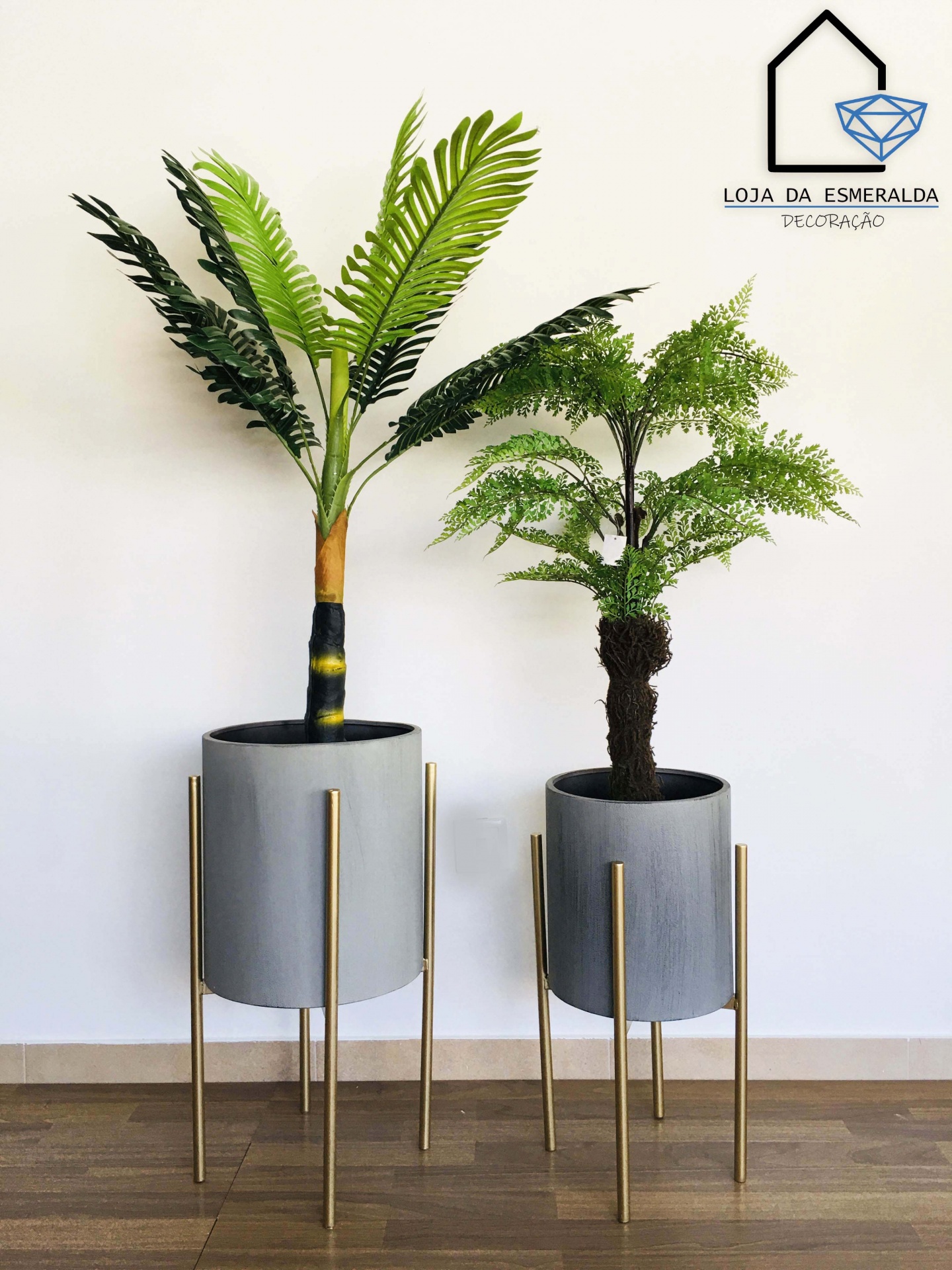 Vasos de plantas artificiais com base metálica dourada em ambiente interior com fundo branco
