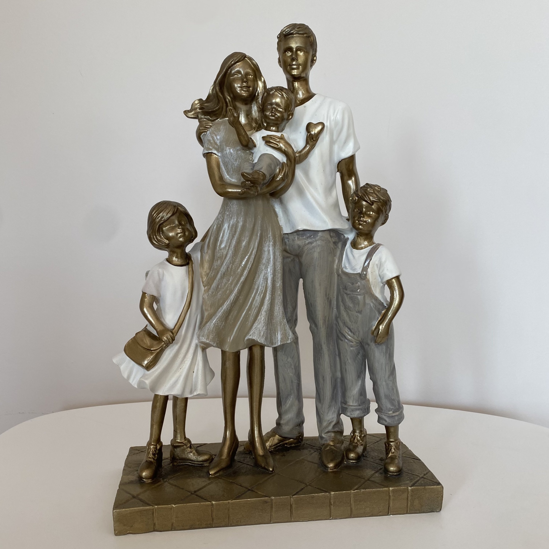 Estátua de família com dois adultos e três crianças em cores bronze, branco e cinza.