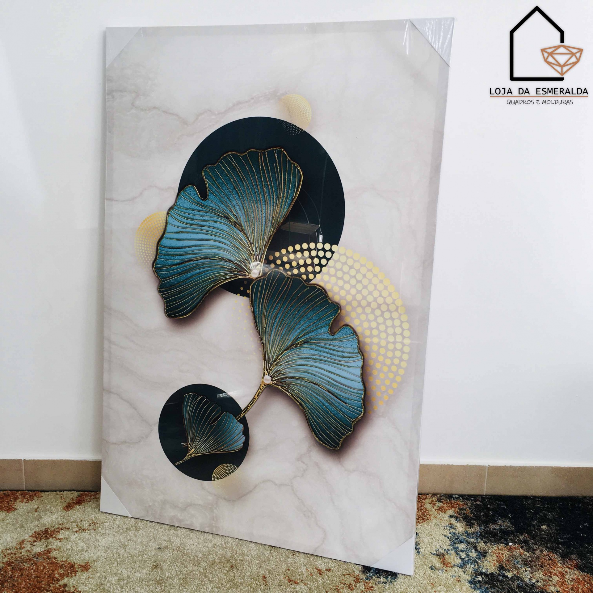 Quadro decorativo com folhas azuis e douradas em fundo geométrico e logo Loja da Esmeralda