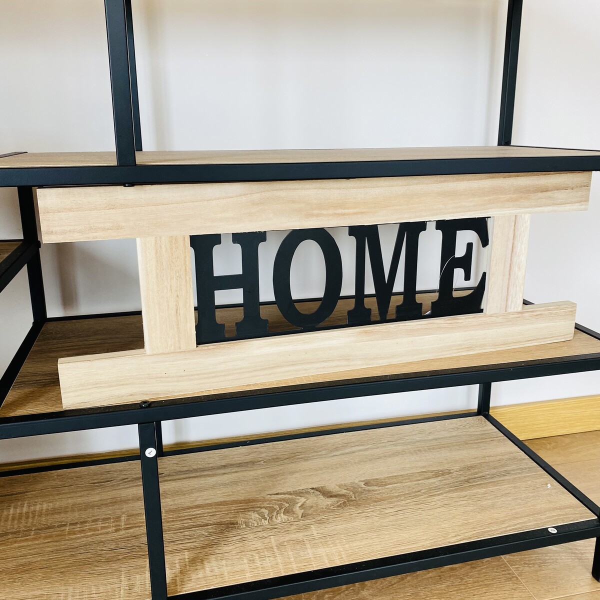 Estante de metal preto e madeira clara com suporte decorativo 'HOME'