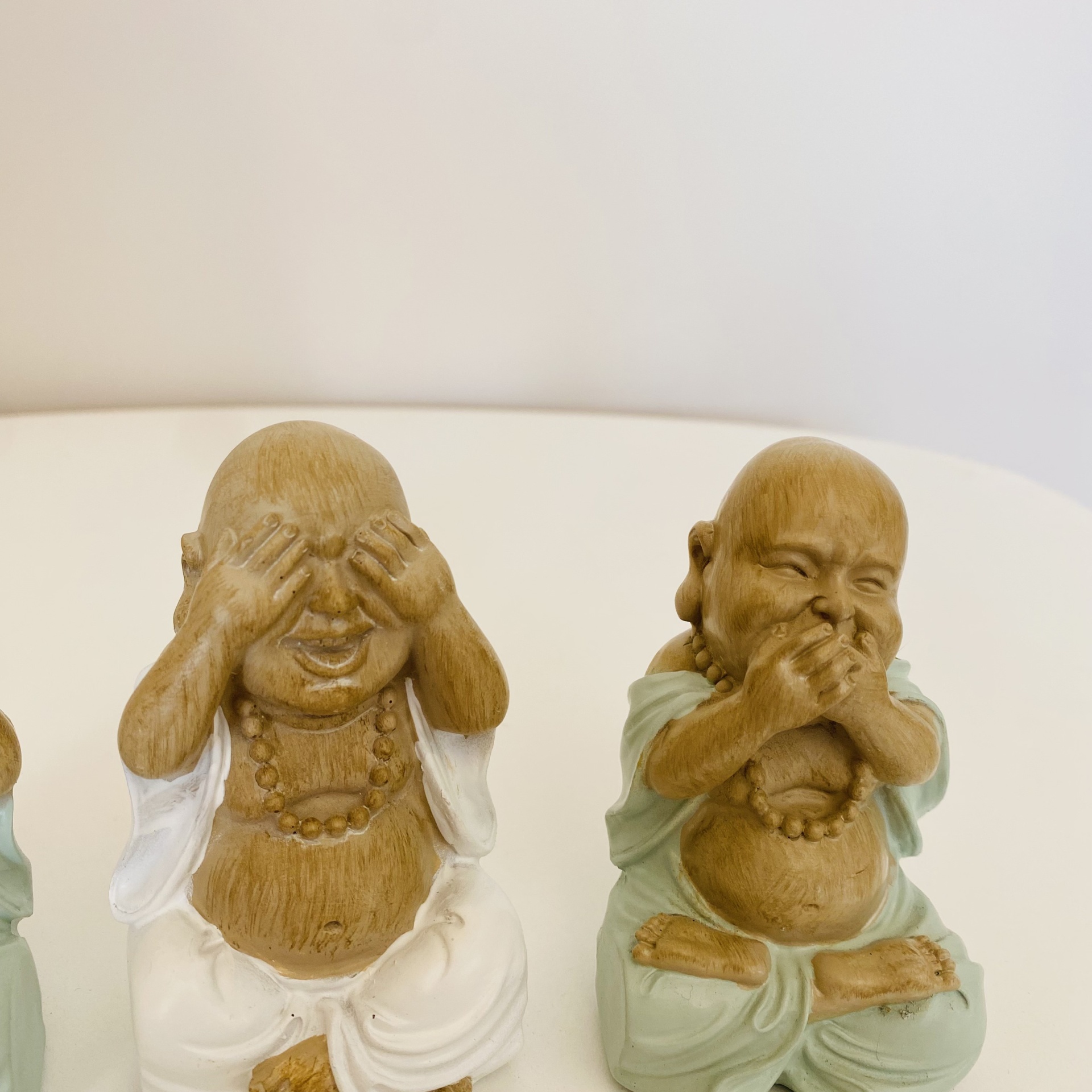 Duas estatuetas de buda sorridentes, uma cobre os olhos, outra cobre a boca, roupas pintadas de branco e verde
