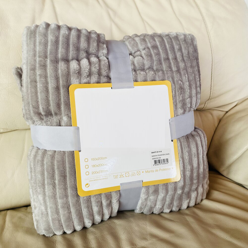 Manta cinzenta acanalada com rótulo e fita cinzenta numa superfície de couro bege