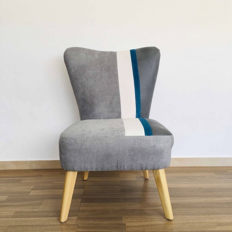 Cadeira cinzenta com faixa branca e azul, pernas de madeira clara, em chão de madeira e parede branca.