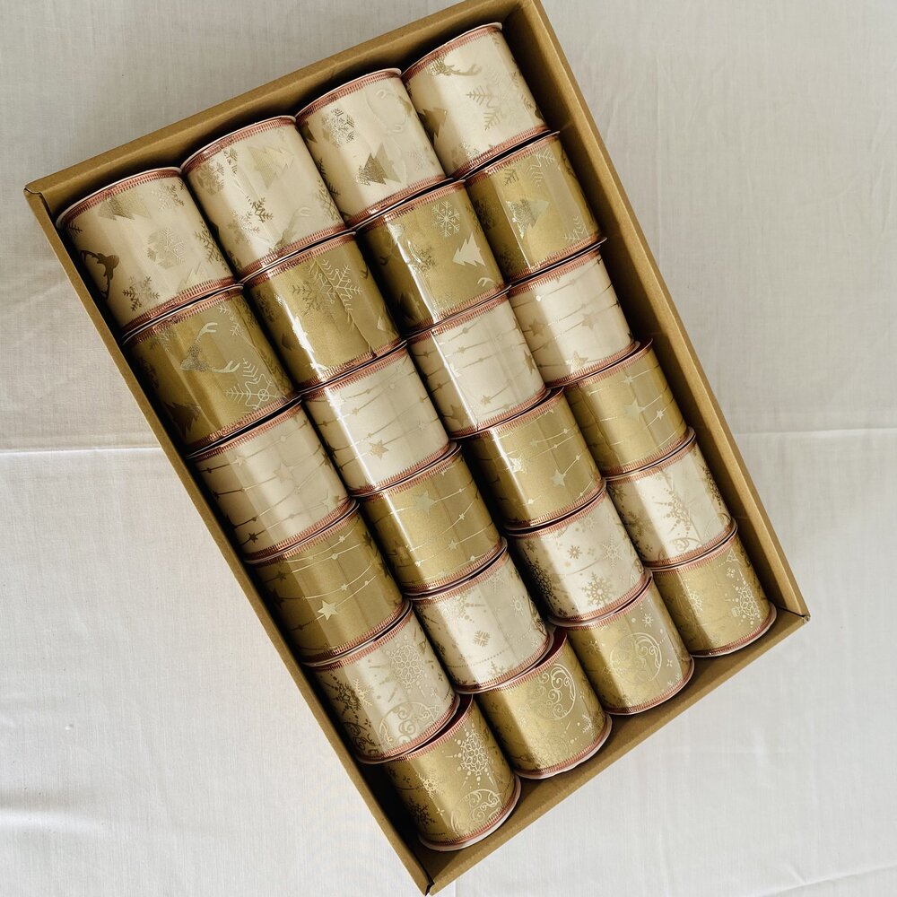 Rolos de fita decorativa creme e dourada com motivos natalícios numa caixa castanha