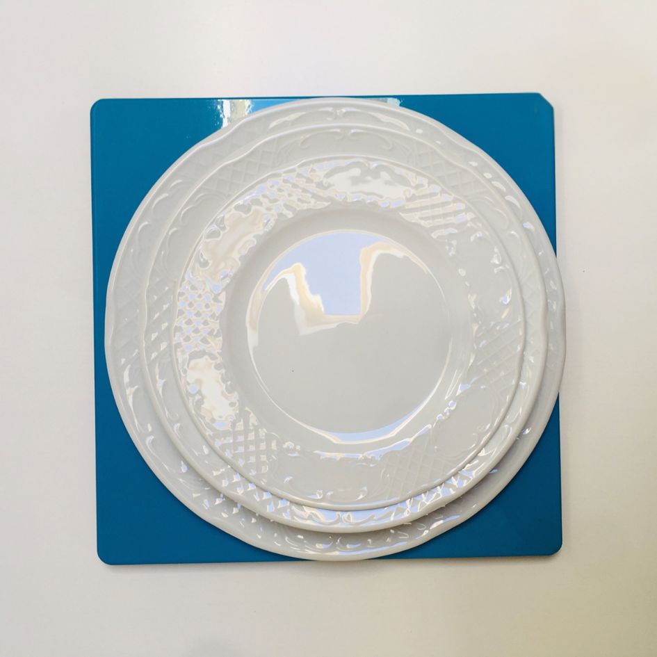 Três pratos brancos em cerâmica com padrão em relevo sobre base azul.