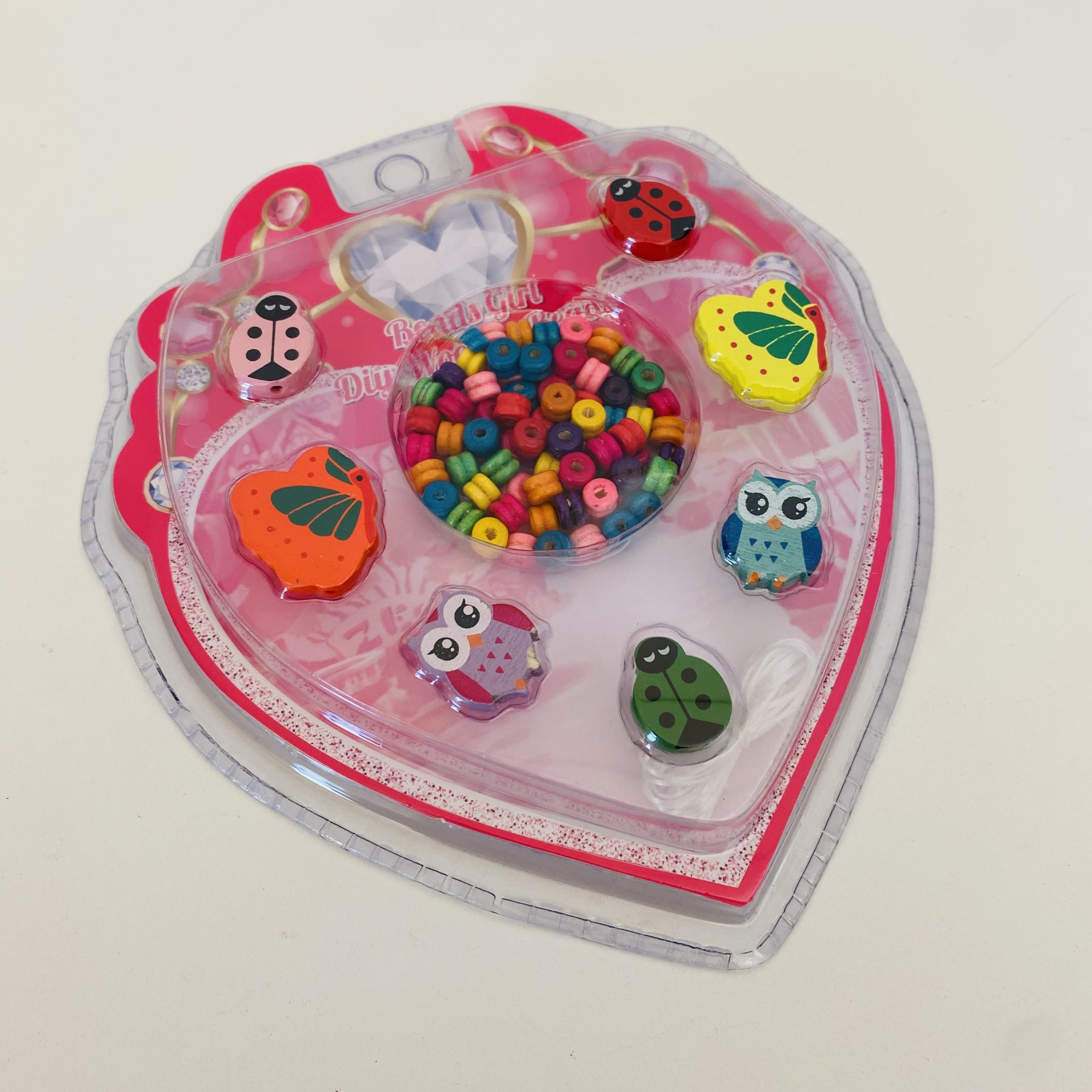 Pacote plástico em forma de coração com miçangas coloridas e anéis decorativos de animais