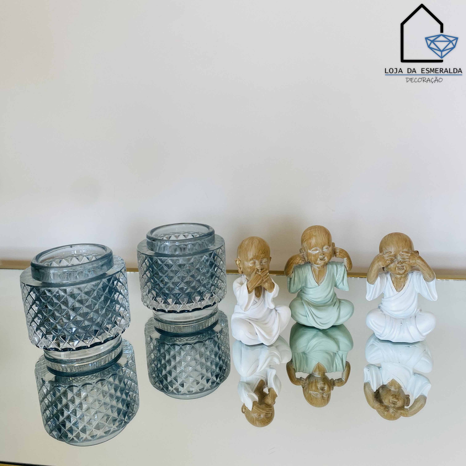 Velas em vidro com padrão e três estatuetas de figuras humanas em diferentes cores sentadas.