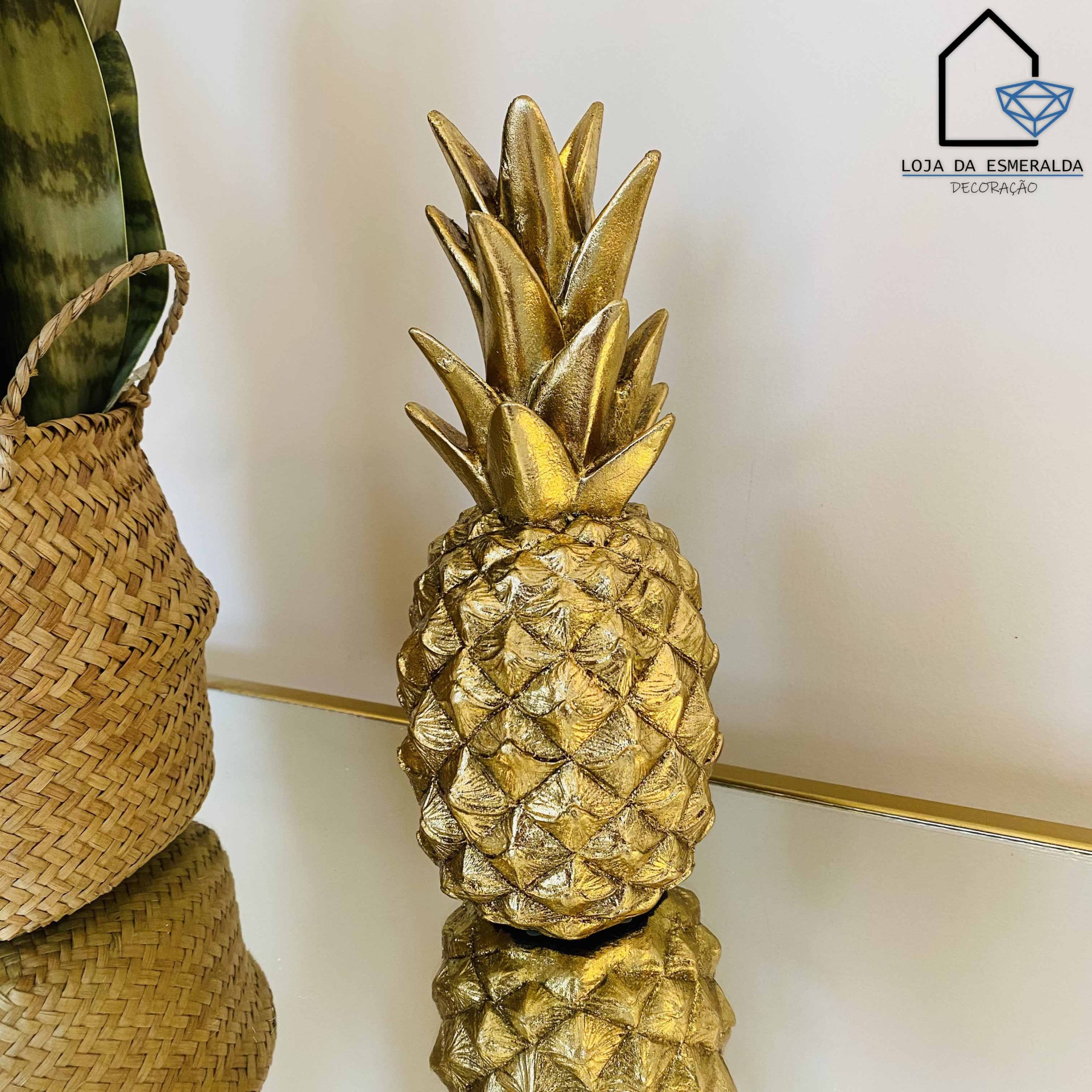 Estatueta dourada de ananás com planta ao lado