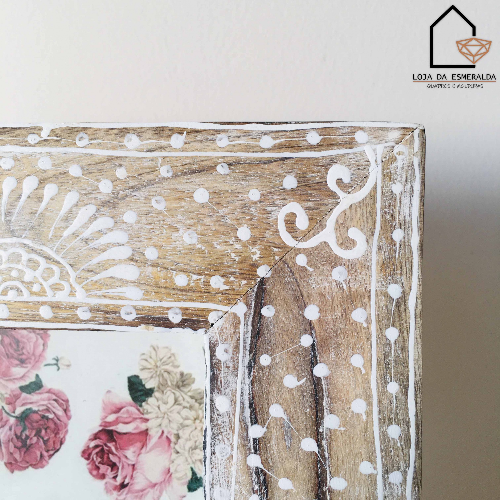 Canto de moldura de madeira pintada com padrão branco e parte de imagem floral com texto Loja da Esmeralda