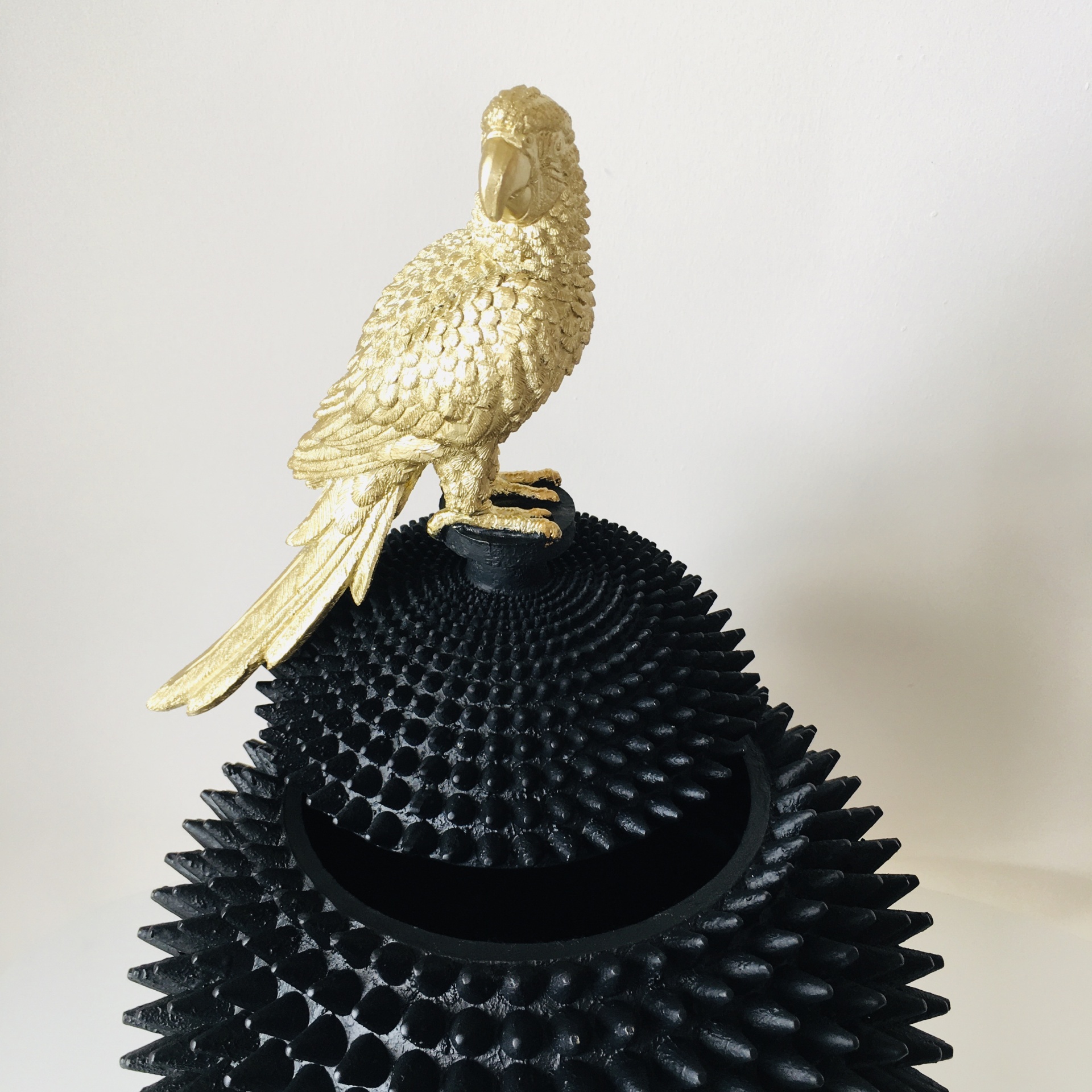 Escultura de papagaio dourado sobre objeto preto com textura pontiaguda