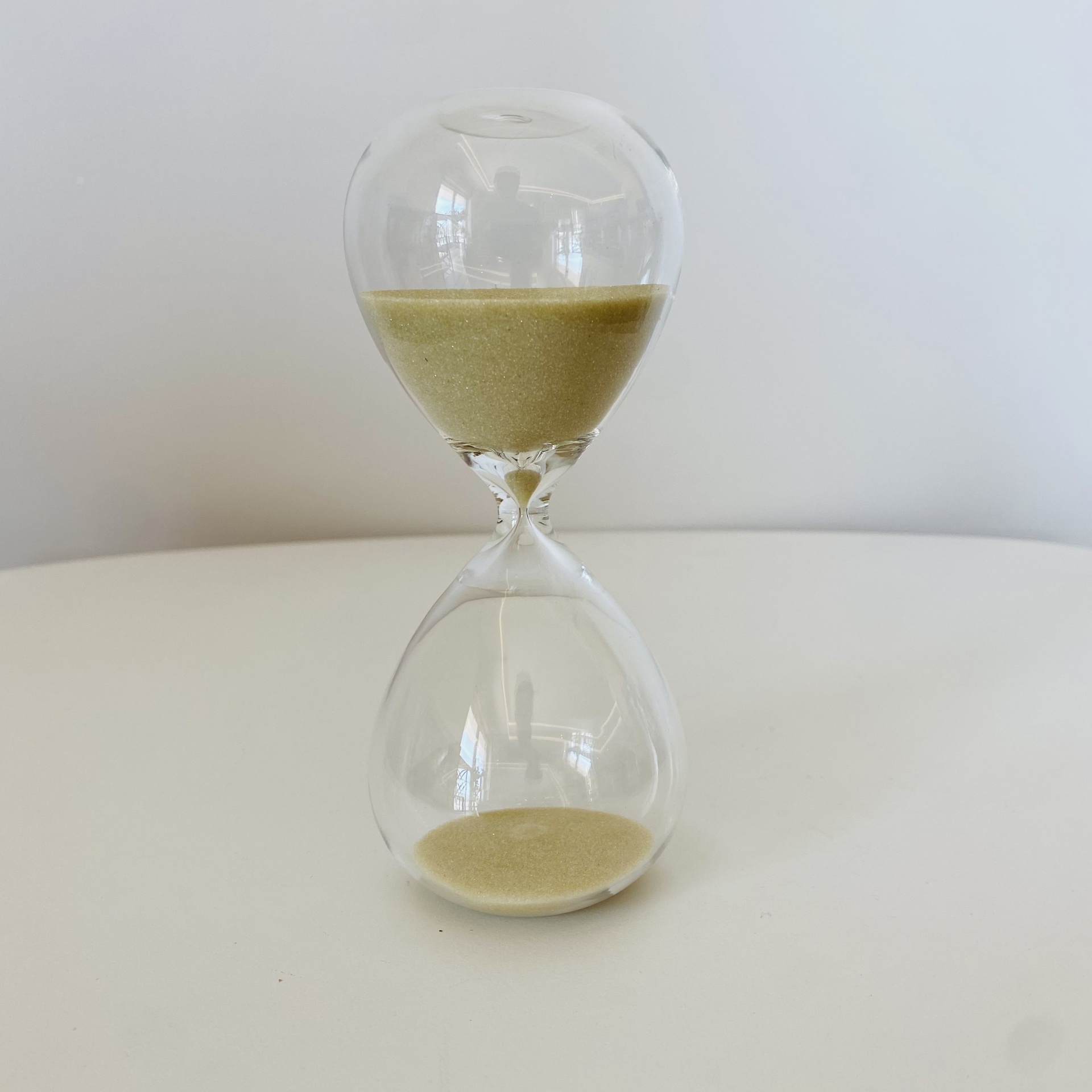 Ampulheta transparente com areia amarela numa superfície branca