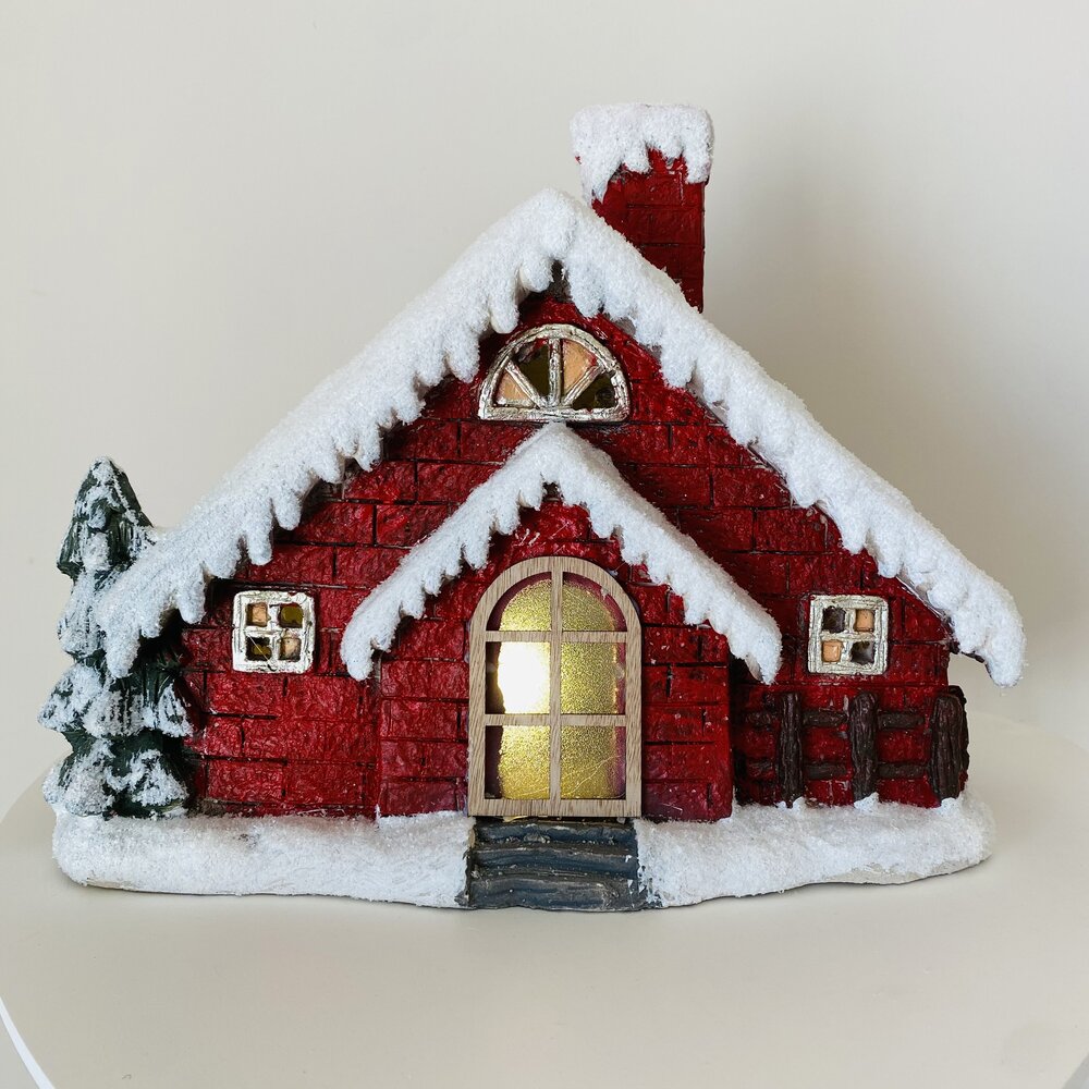 Miniatura de casa vermelha com neve artificial e árvore verde ao lado