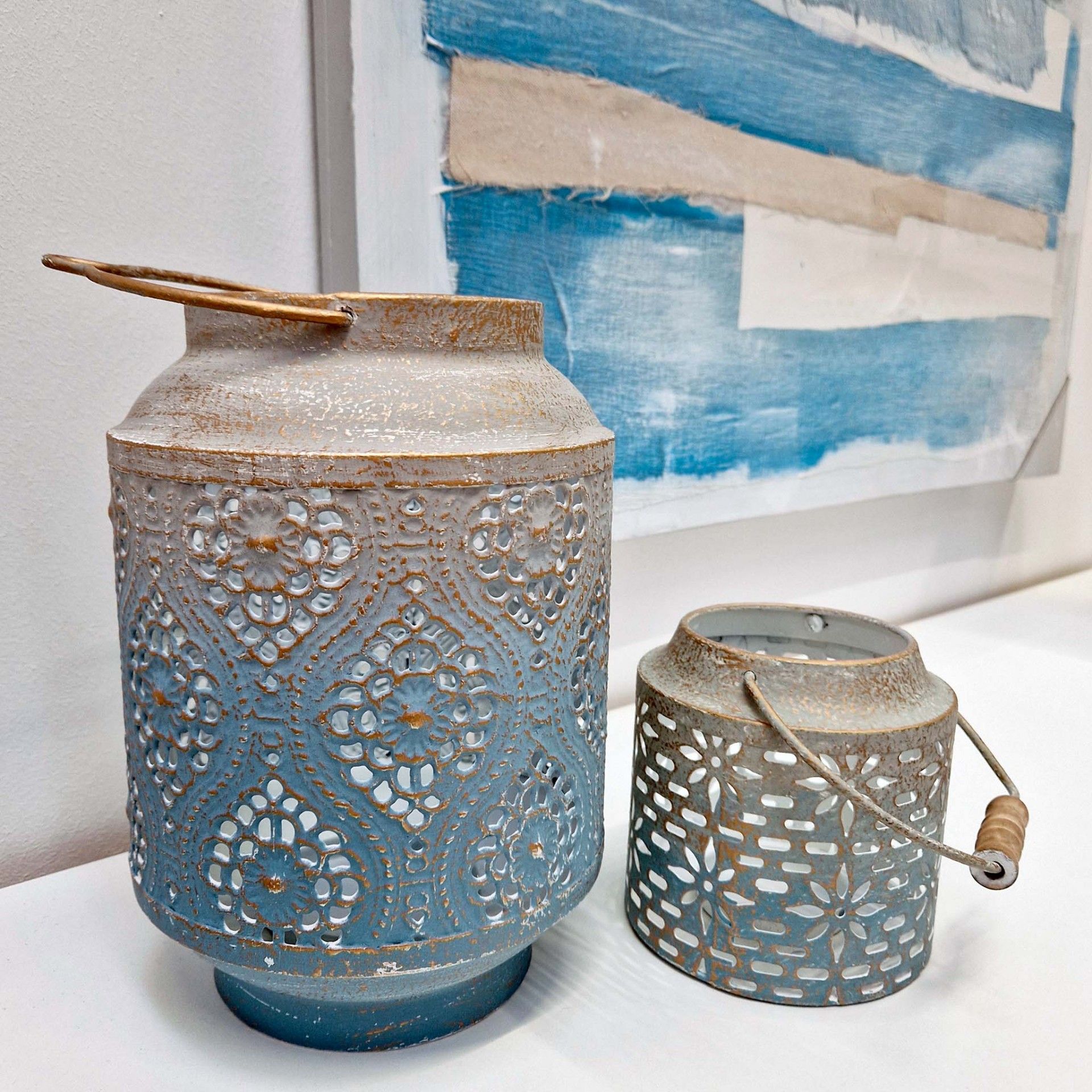 Dois castiçais em metal azul com padrões recortados e alças de couro em superfície branca