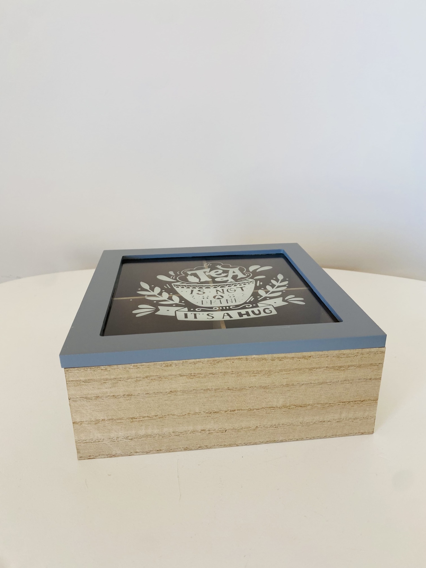 Caixa de madeira clara com moldura azul e tampa de vidro com texto decorativo