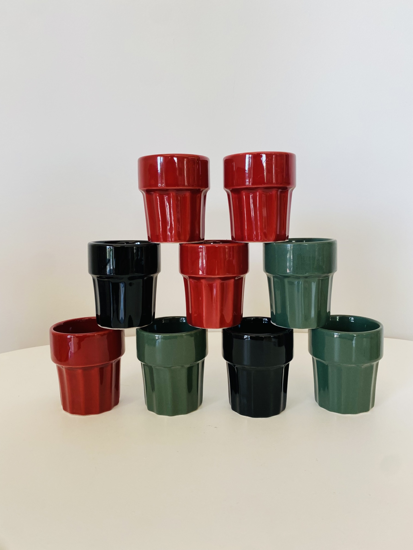 Nove copos cerâmicos brilhantes empilhados em pirâmide, cores vermelho, verde e preto.