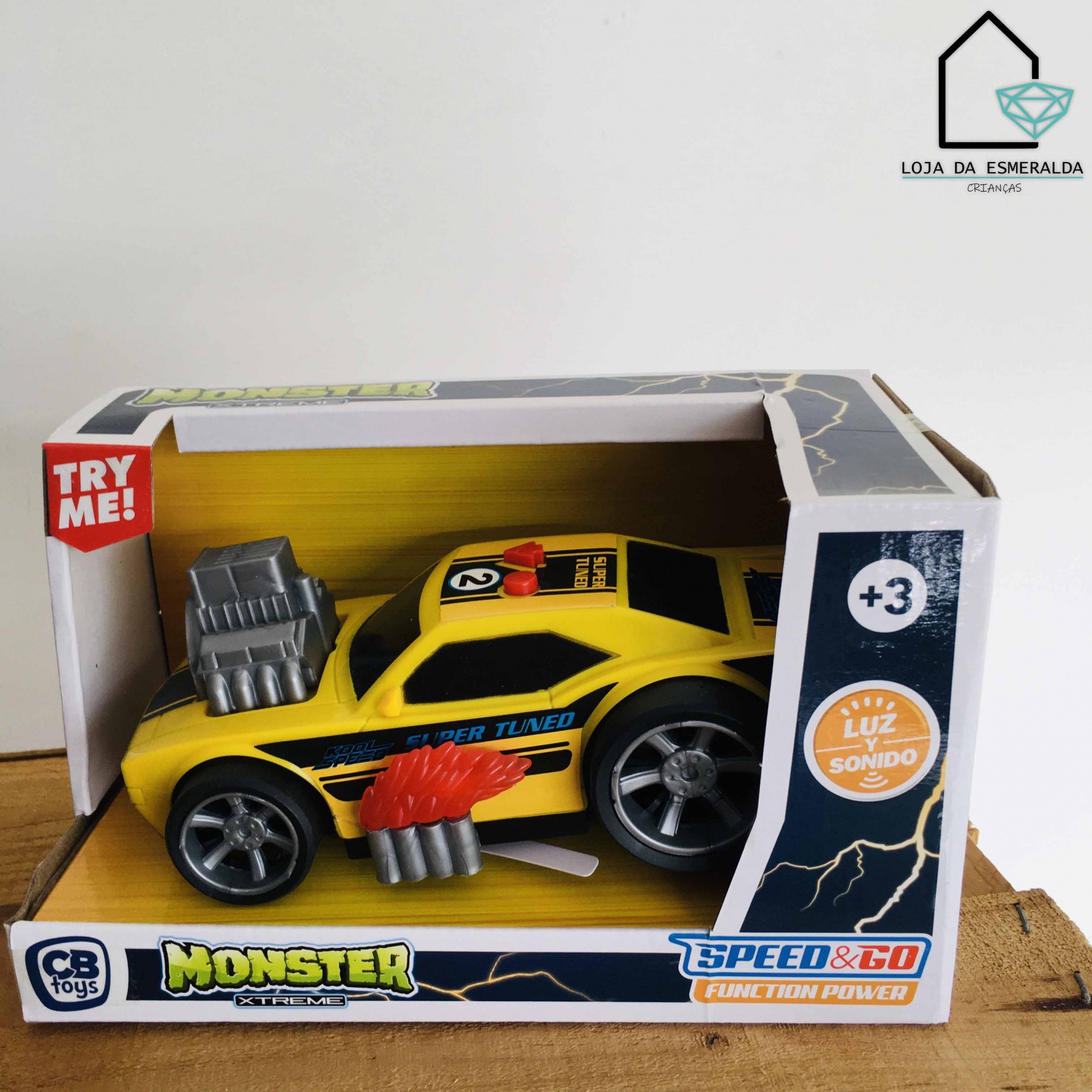 Brinquedo de carro amarelo com detalhes pretos e motor cinza na embalagem com informações e padrão de raios