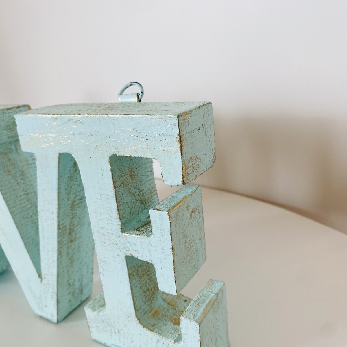 Letra decorativa de madeira azul claro desgastada em fundo branco.