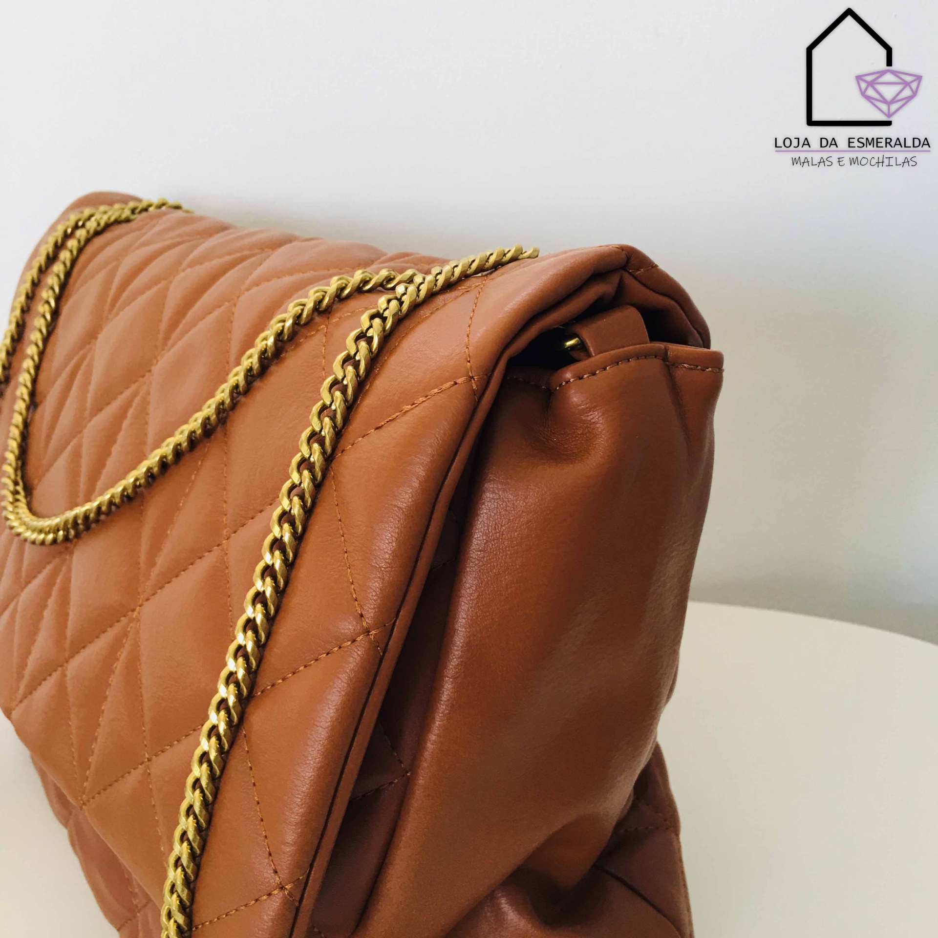 Mala castanha acolchoada com alça dourada sobre superfície branca