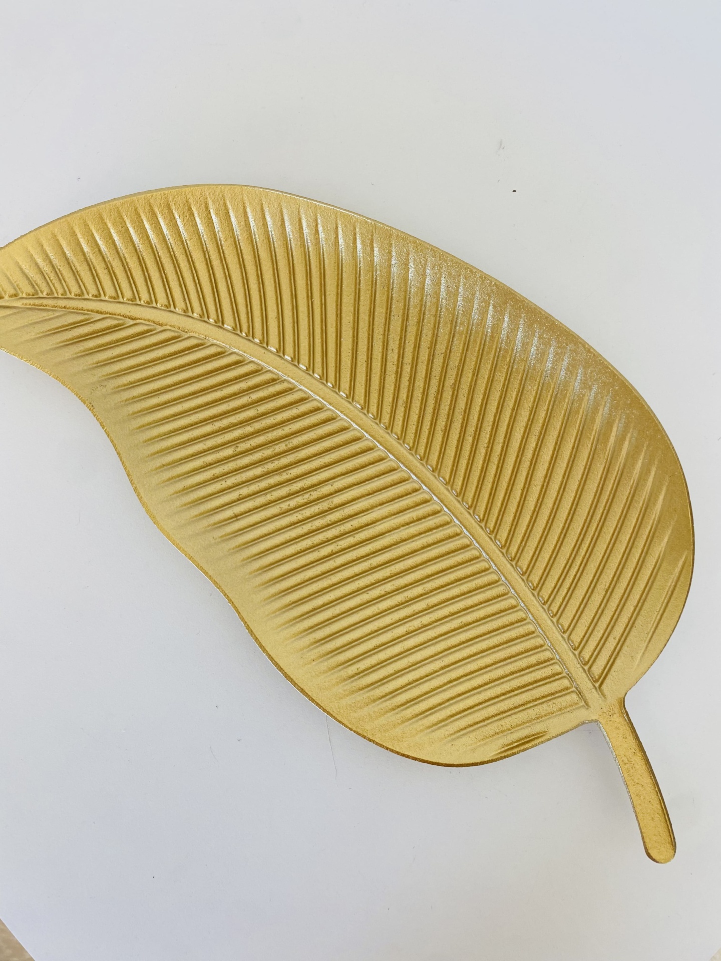 Prato decorativo dourado em forma de folha com textura de nervuras.