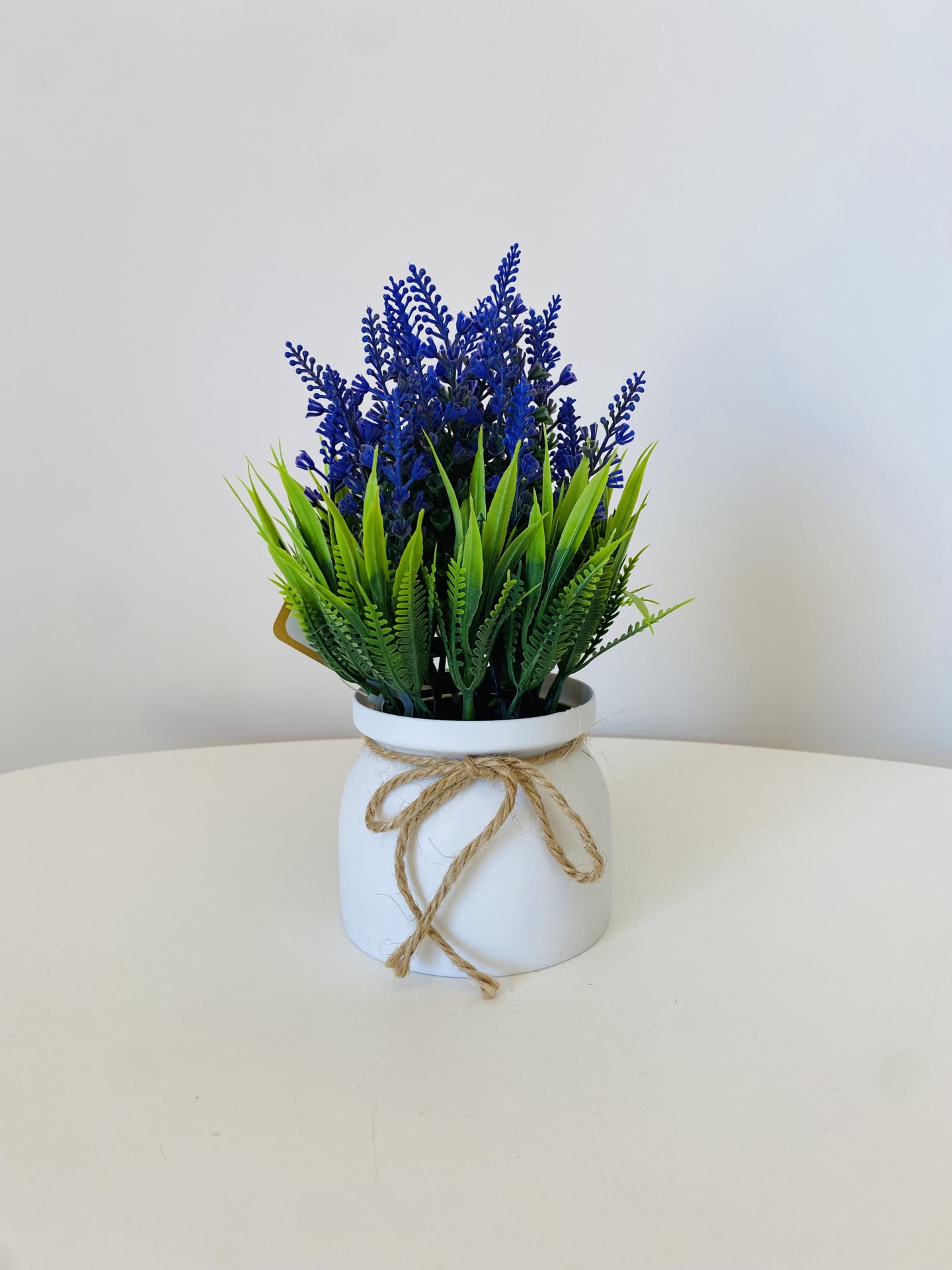 Vaso branco com planta artificial verde e roxa sobre mesa branca